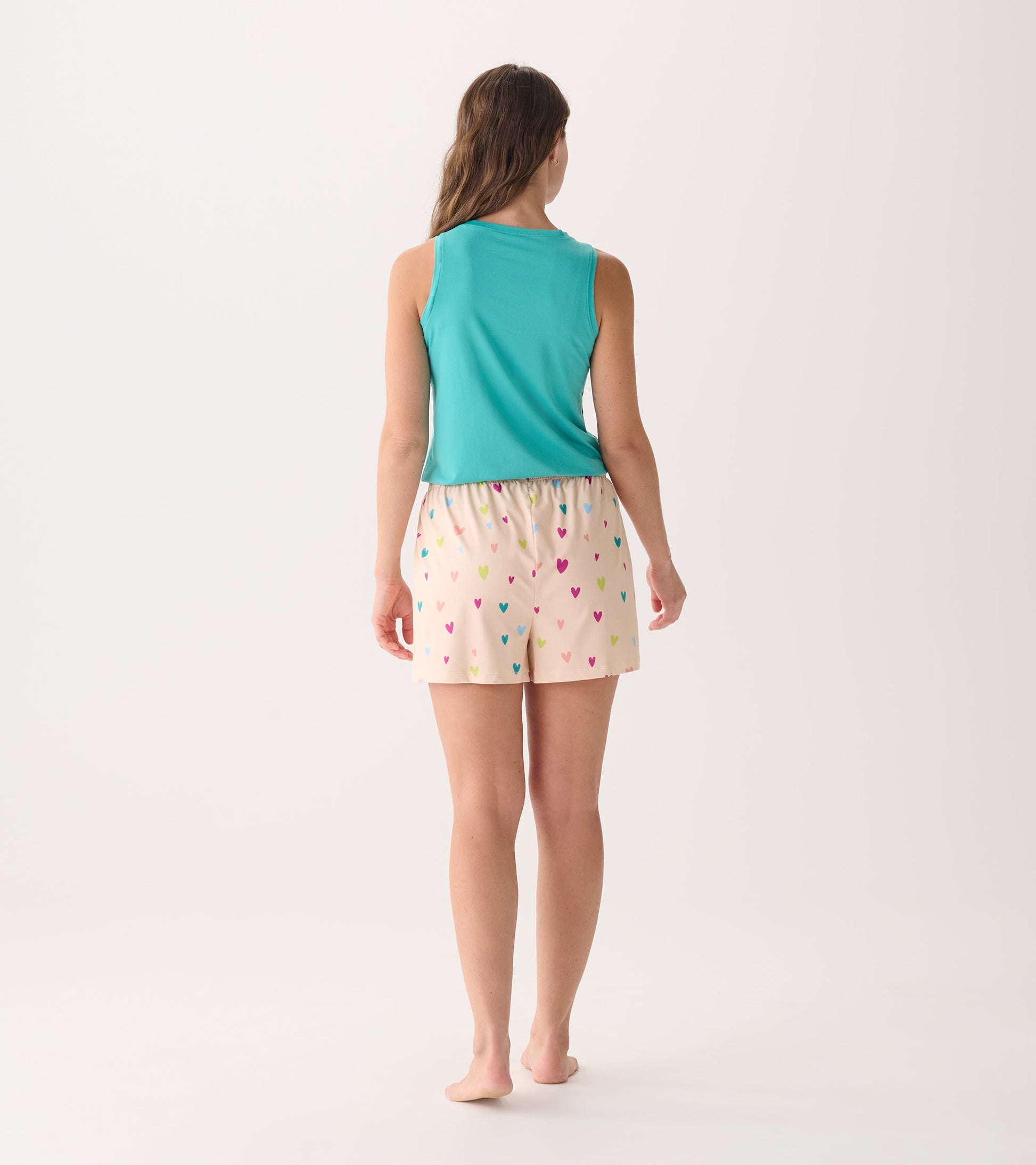 Back view of a woman wearing teal sleeveless top and cream shorts with colorful heart patterns.