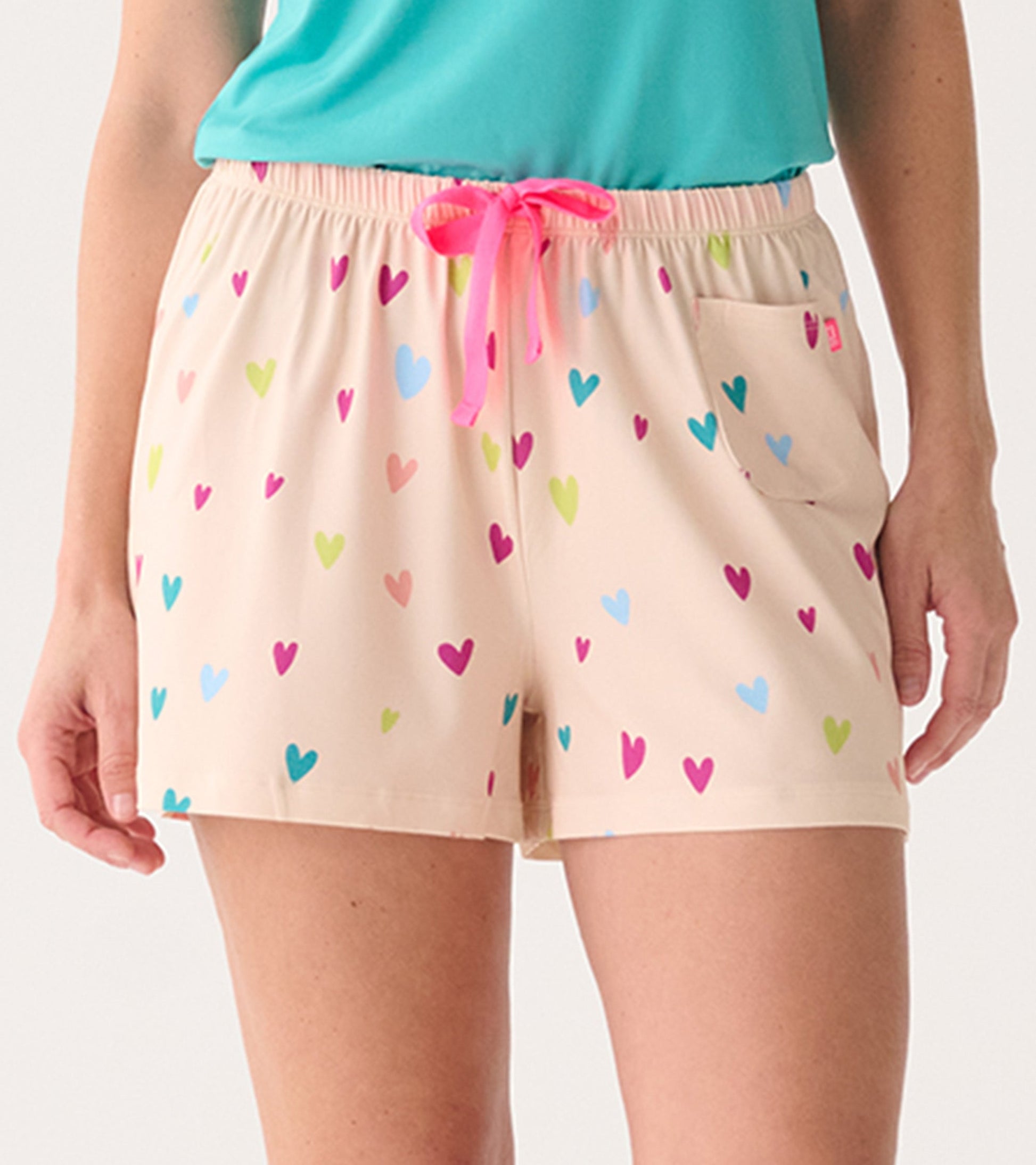 Peach pajama shorts with colorful heart patterns and a pink drawstring, featuring a side pocket.