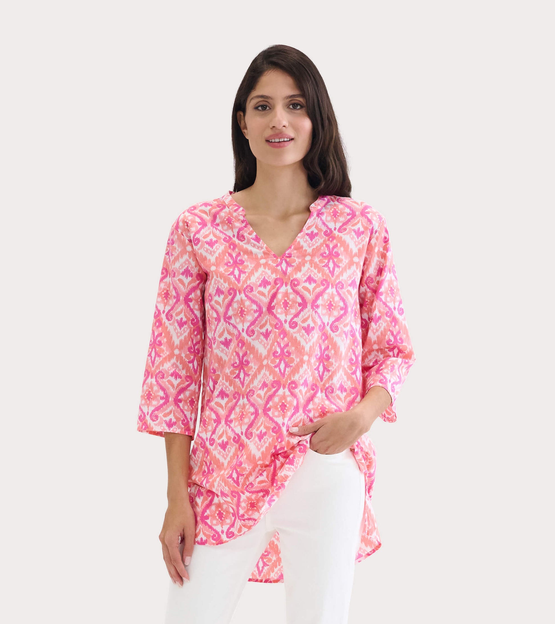 Pink and white patterned tunic with a V-neck and three-quarter sleeves, styled with white pants.