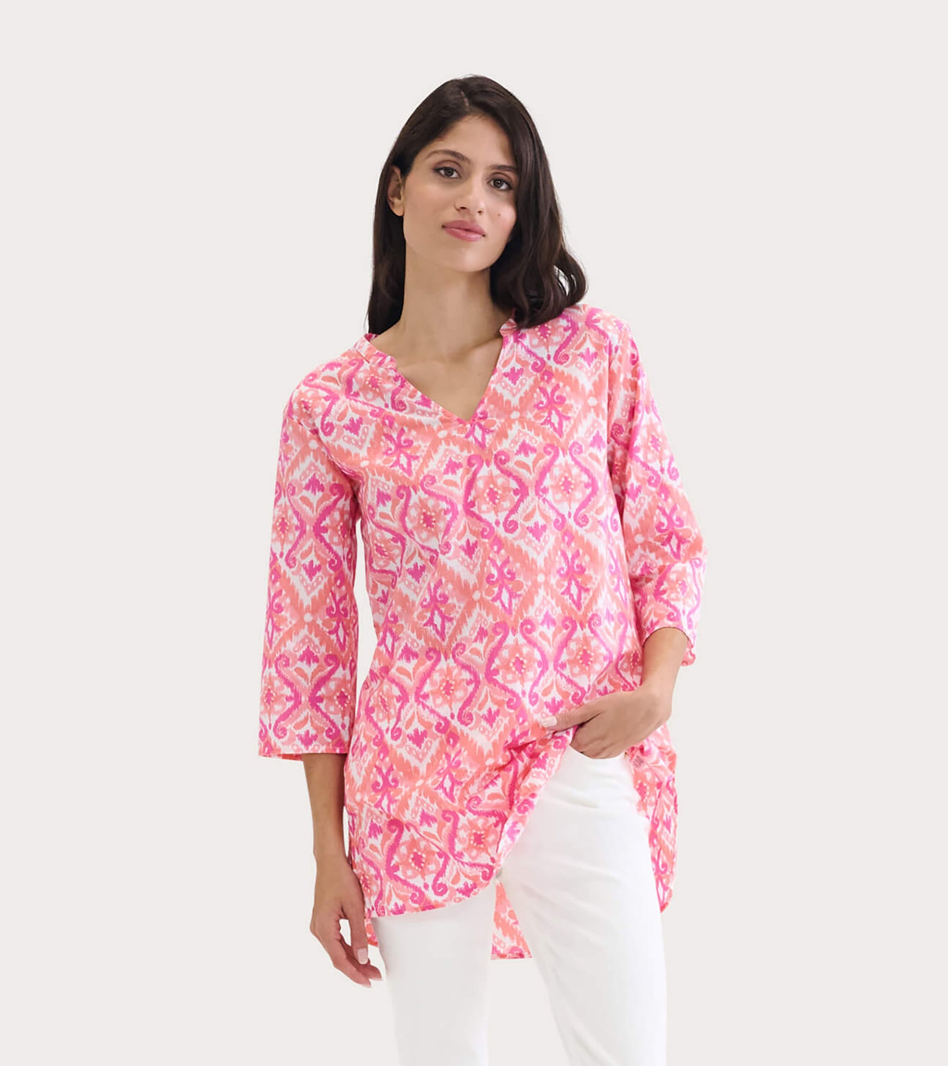 Pink and white patterned tunic with a V-neck and three-quarter sleeves, styled with white pants.
