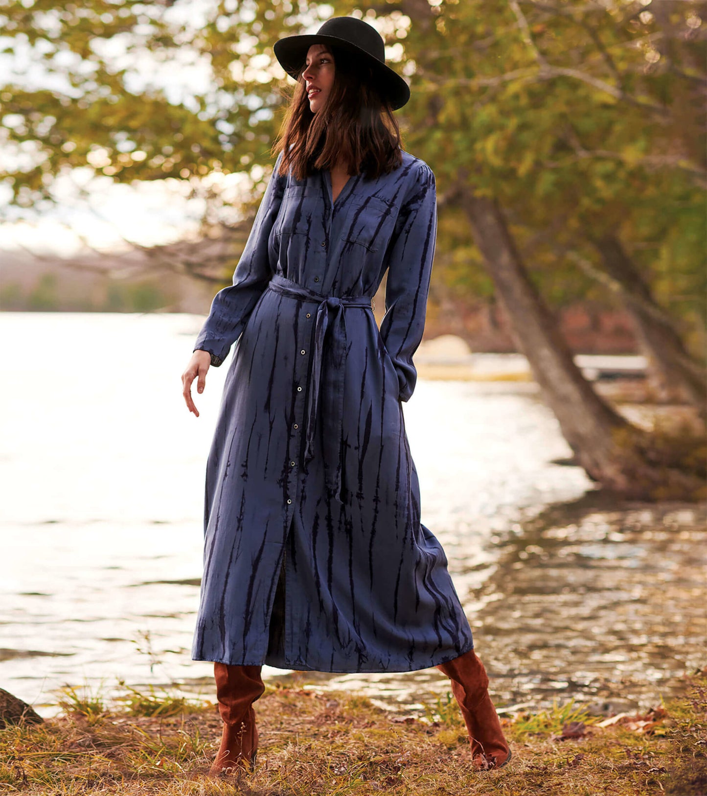 Long-sleeve maxi shirt dress in deep blue with a tie waist and vertical stripes, styled with a black hat and brown boots.