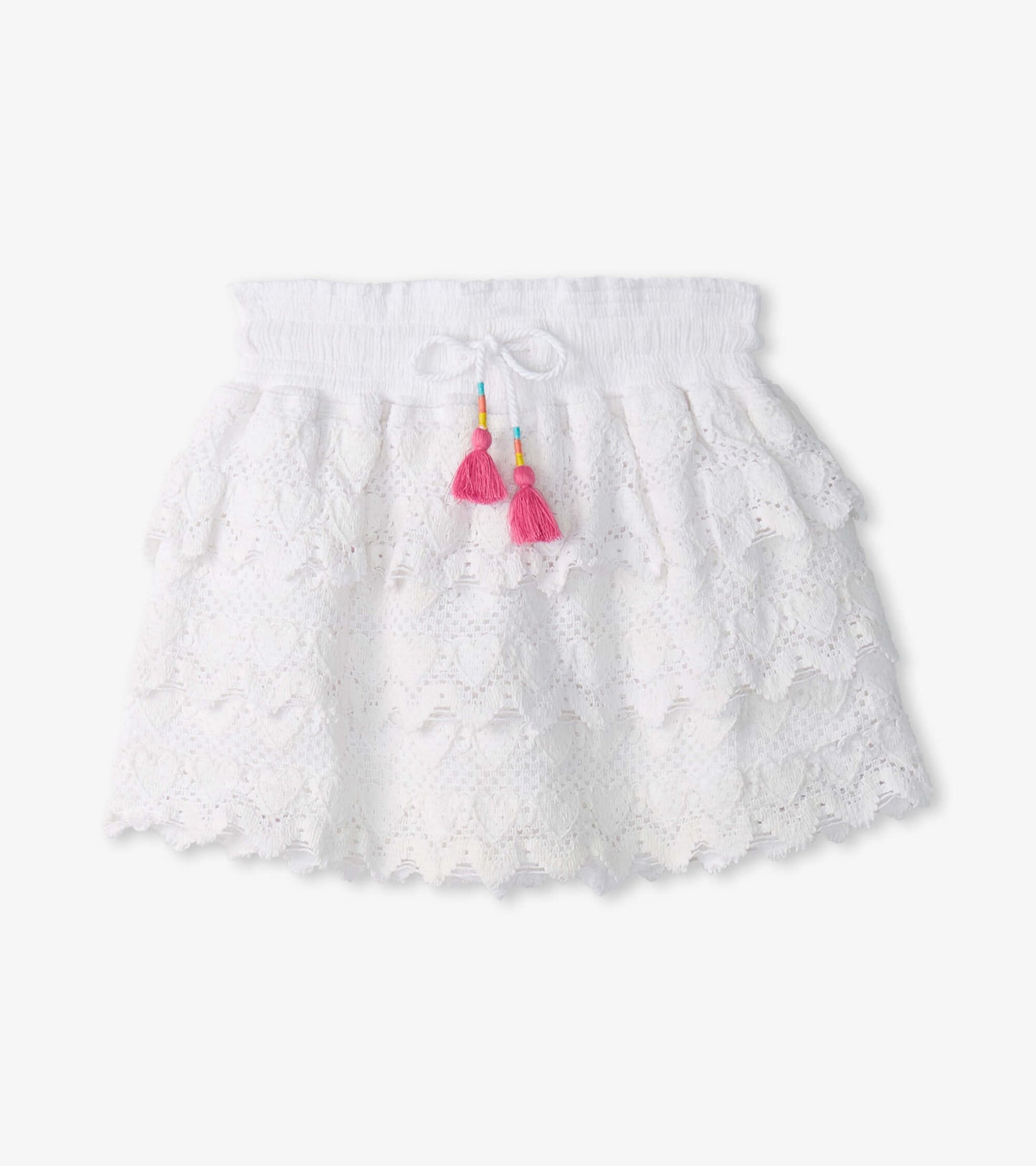 White floaty skort with heart pattern, layered ruffles, and pink tassel accents. Elastic waistband for comfort.