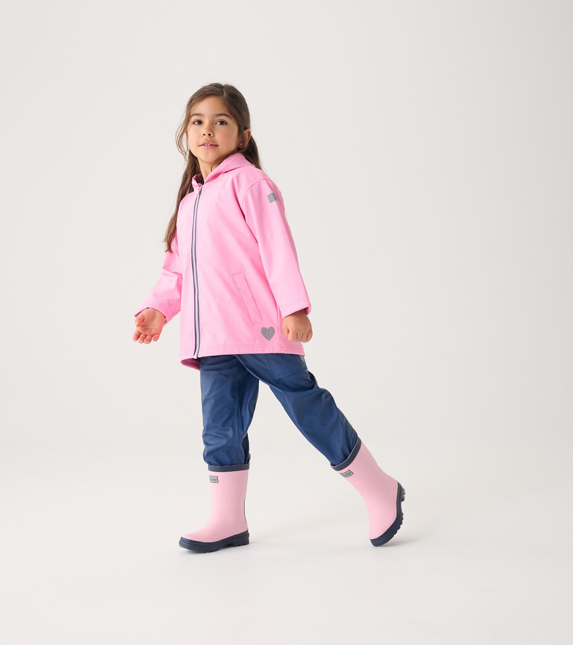 Classic pink zip-up rain jacket with a hood, paired with navy pants and pink rain boots, worn by a girl.