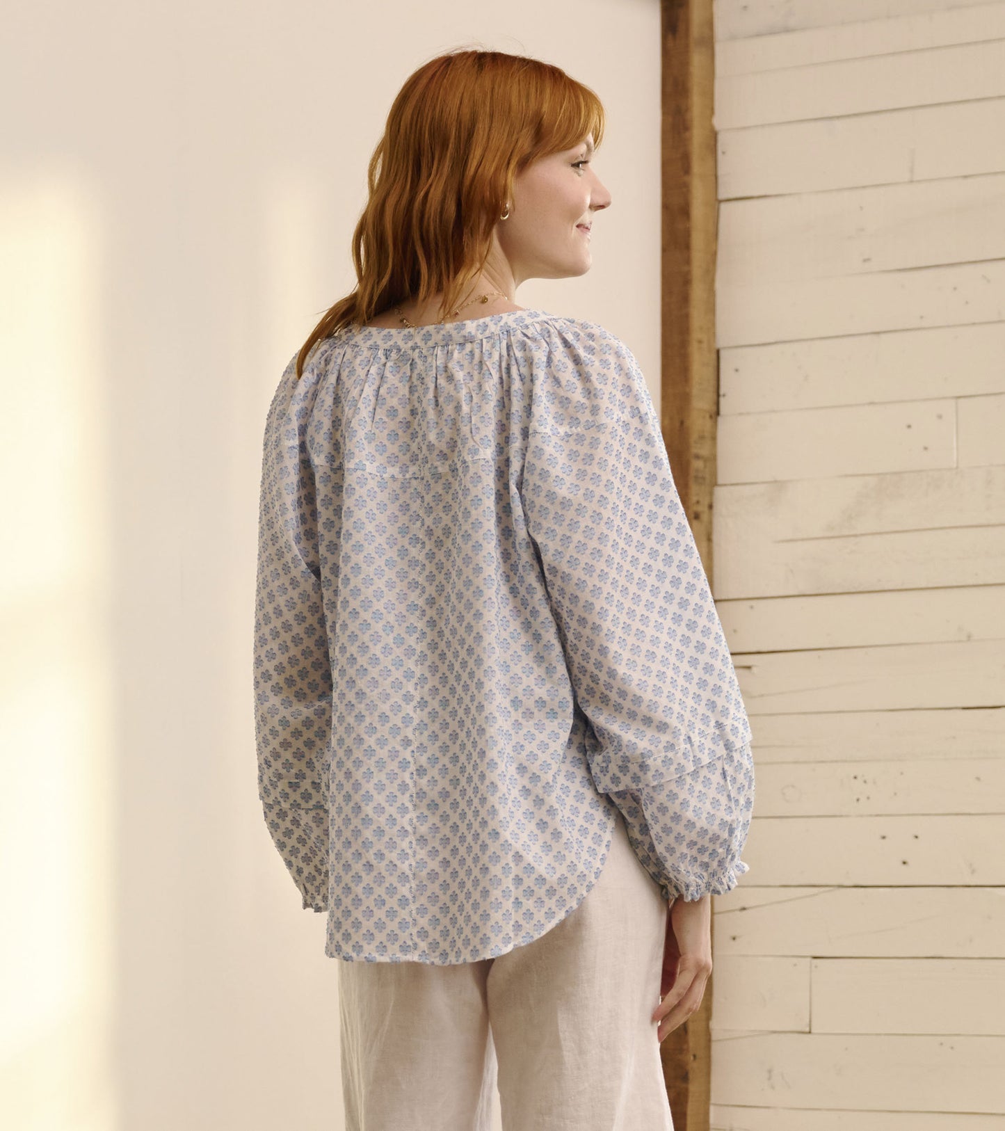 Light blue blouse with floral pattern, gathered neckline, and puffed sleeves, shown from the back.