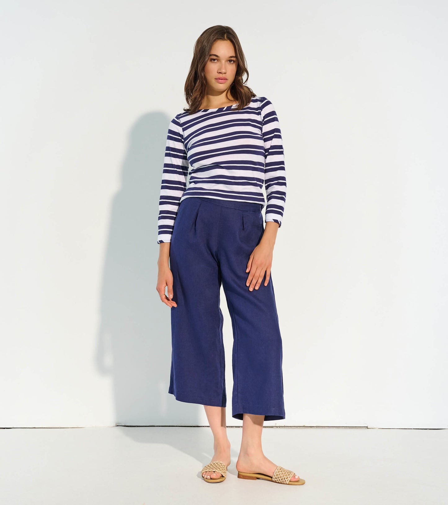 Navy cropped wide leg pants with pleats, styled with a striped top and sandals, standing against a light background.