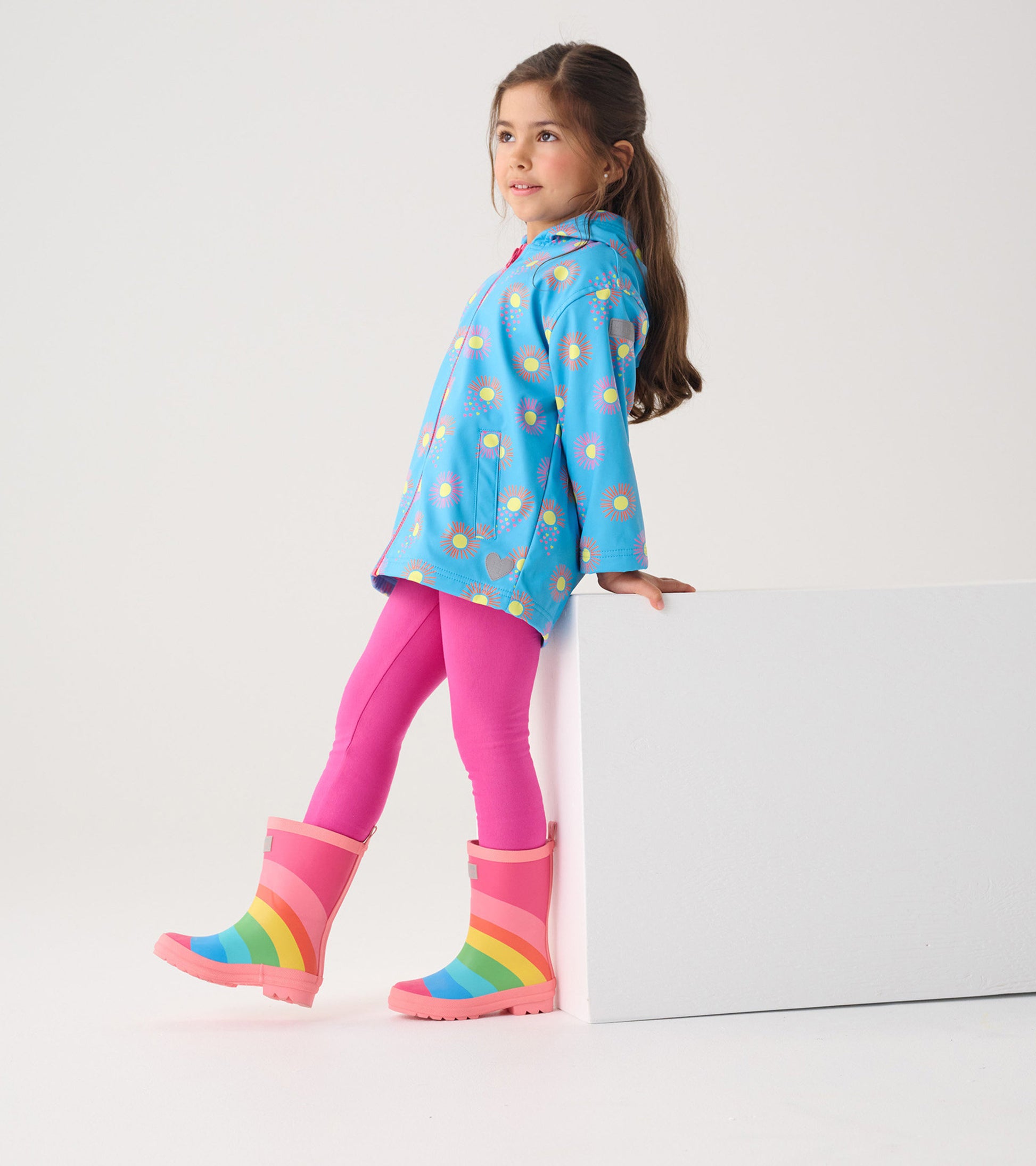 Blue zip-up rain jacket with sun patterns, paired with pink leggings and colorful rainbow rain boots.