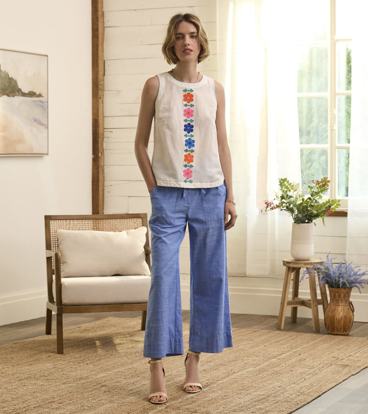 White sleeveless tank top featuring colorful embroidered flowers down the center, paired with light blue wide-leg pants.