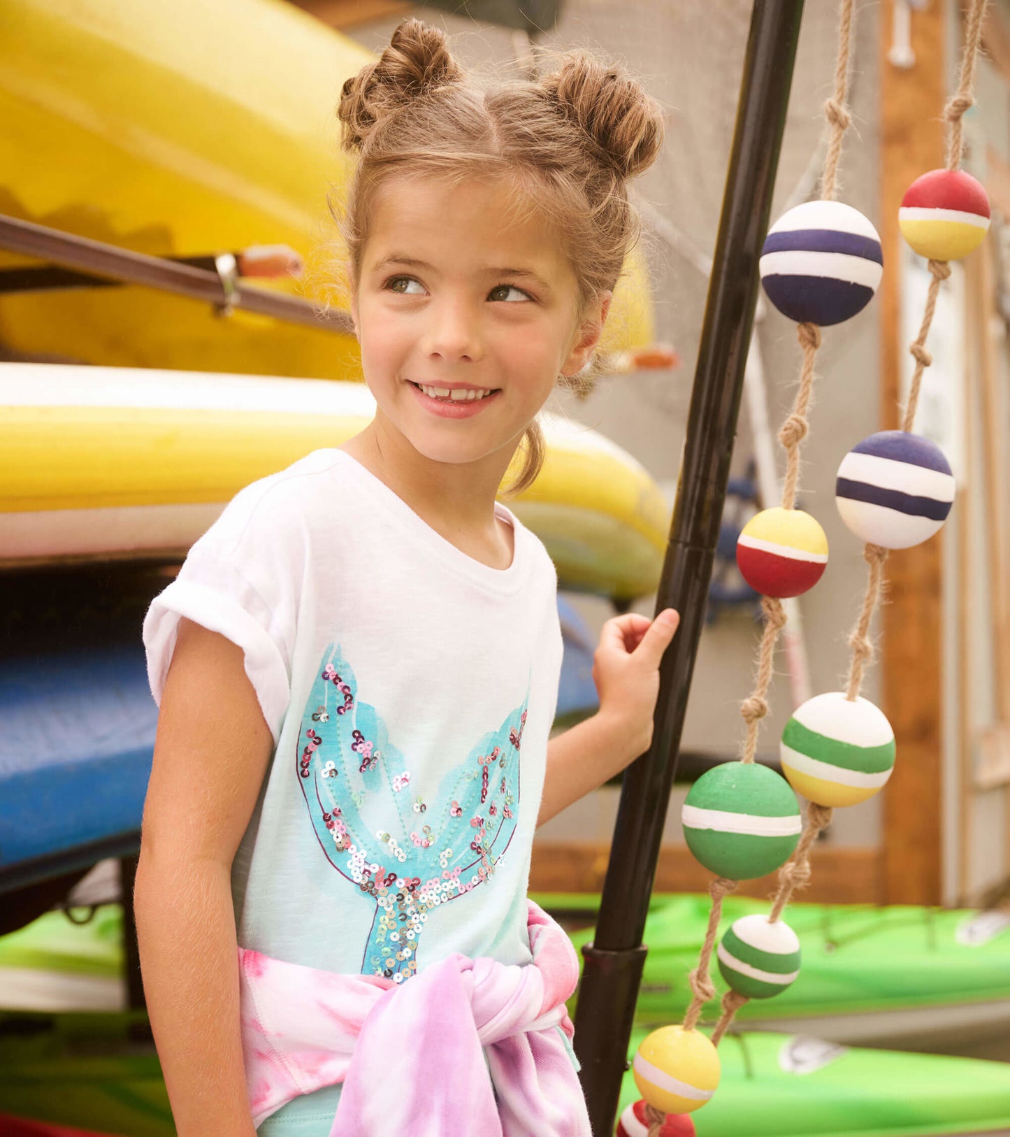 White short-sleeve tee featuring a sparkly turquoise whale tail design, worn by a girl with a pink tie-dye wrap around her w…