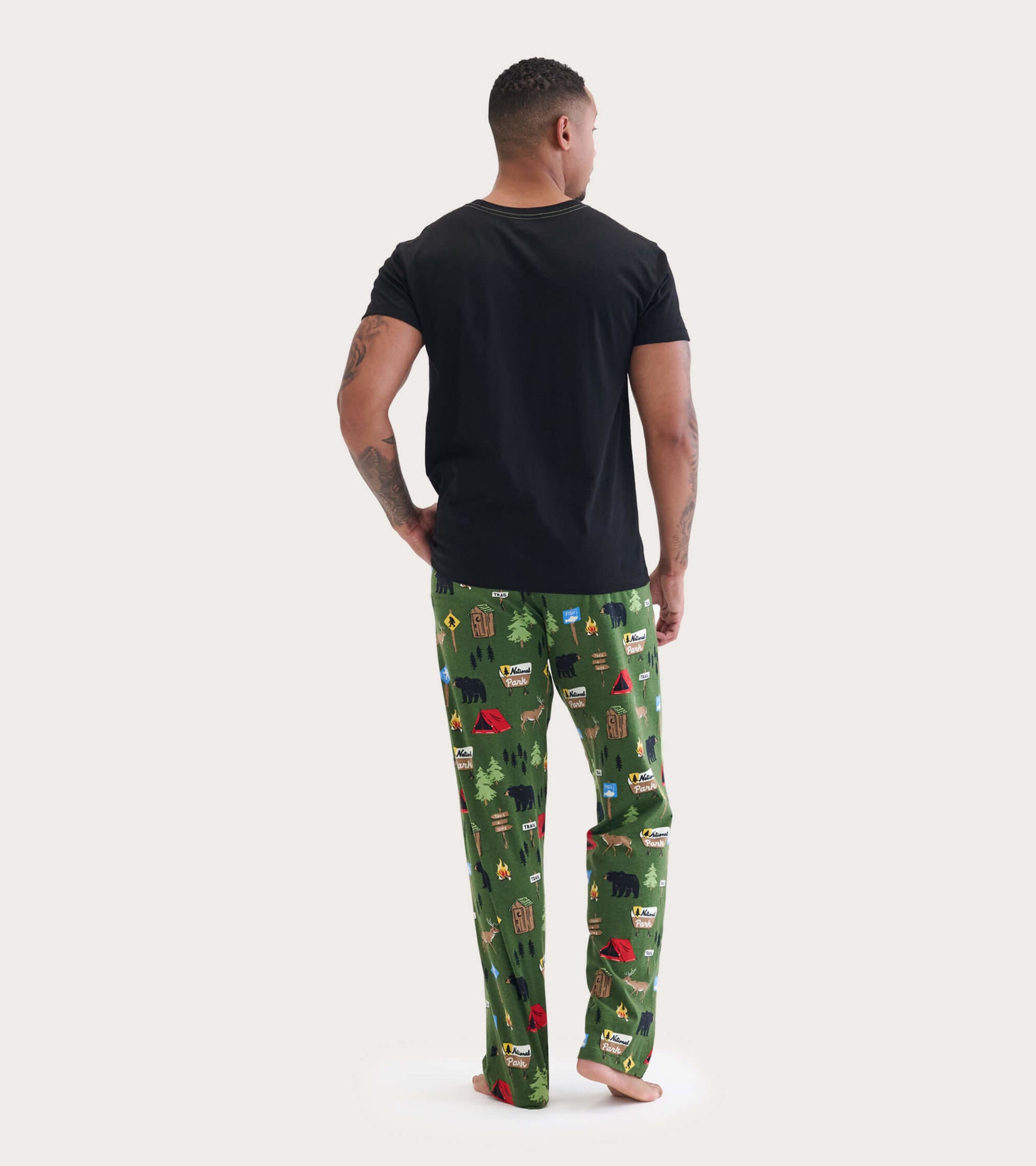 Men's green cotton pajama pants featuring a camping-themed print with trees, bears, and tents, shown from the back.