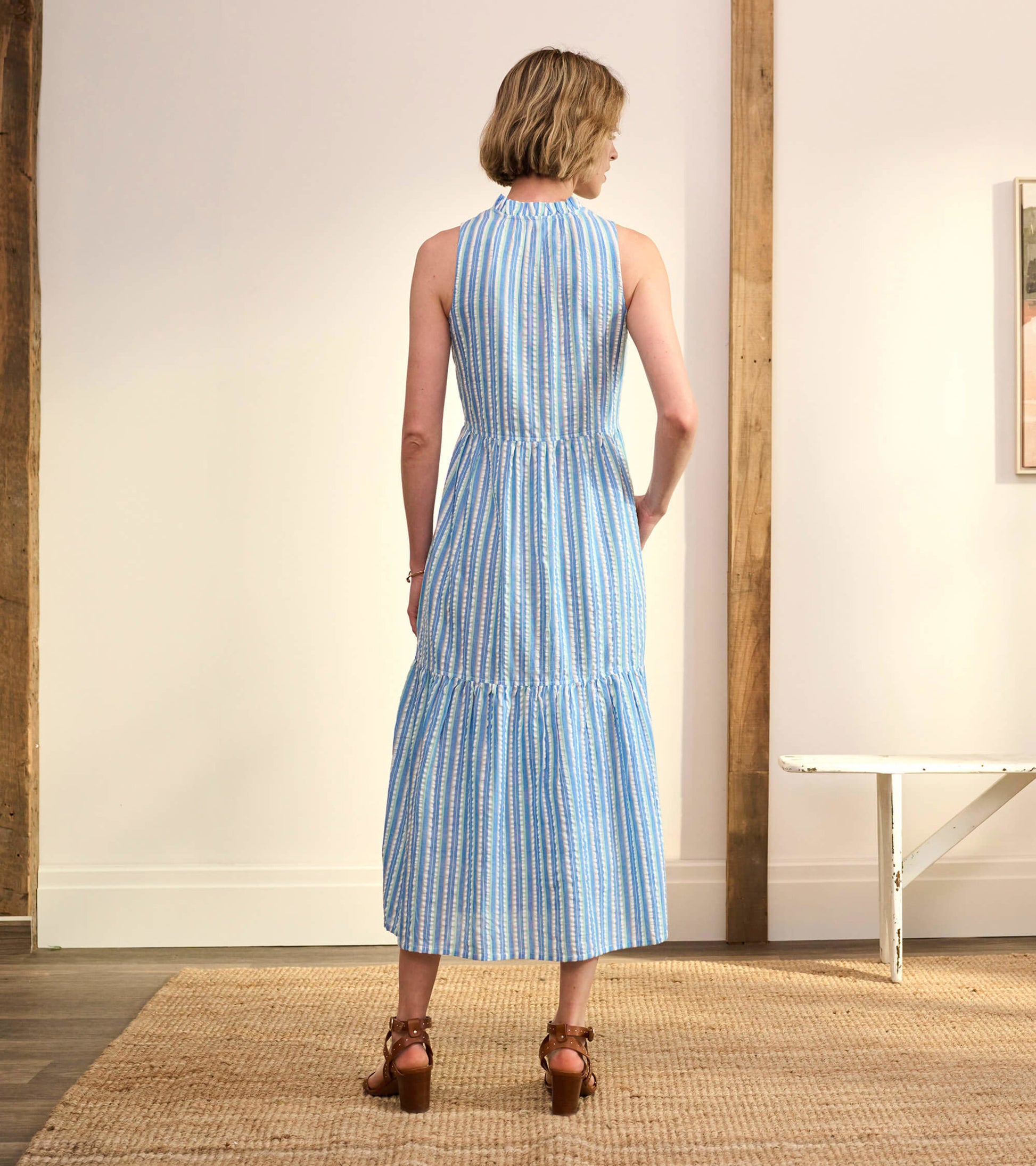 Back view of a blue and white striped seersucker sundress with a tiered skirt and halter neckline.