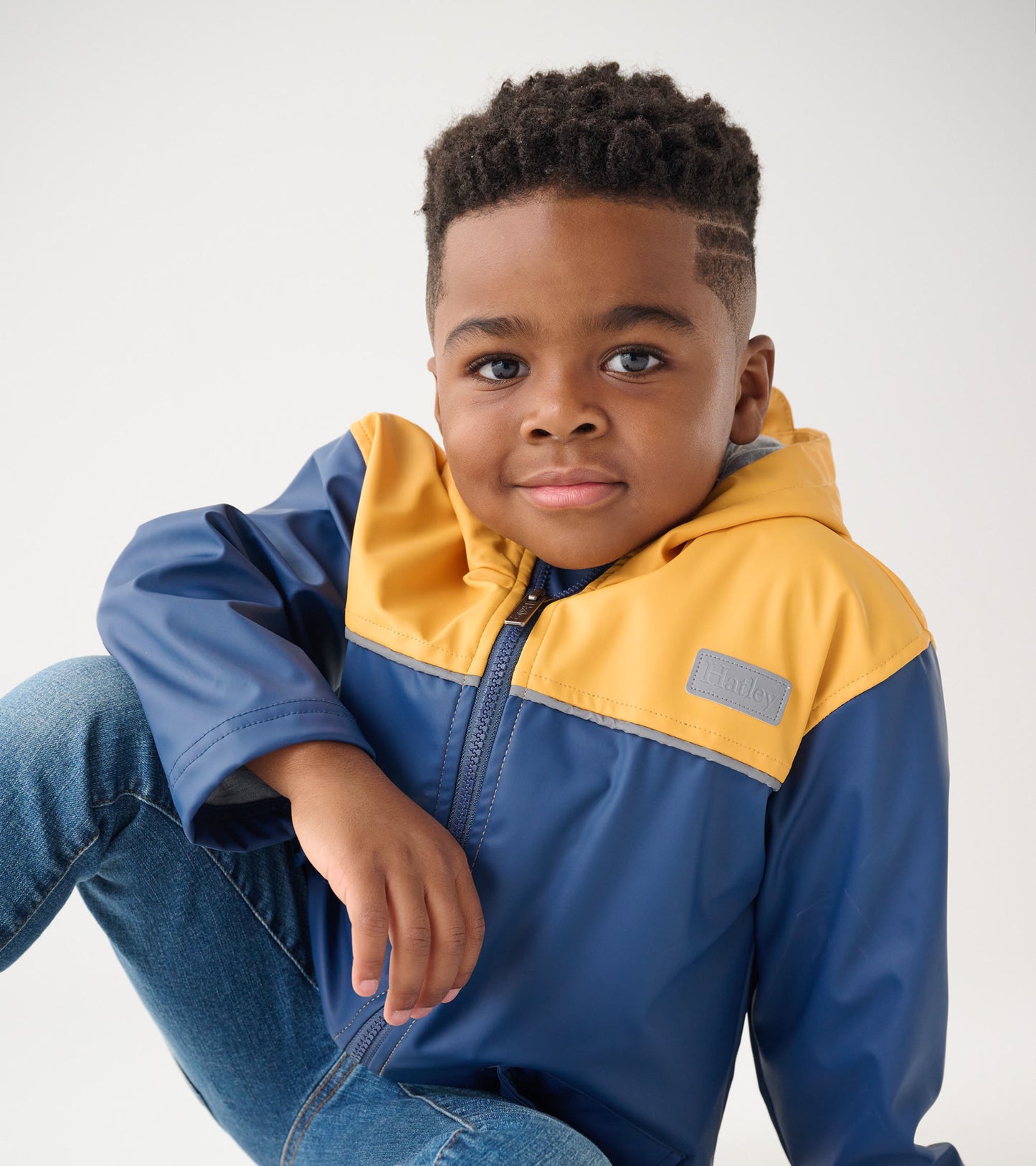 Yellow and navy zip-up rain jacket with a hood, worn by a child, featuring a smooth, waterproof material.