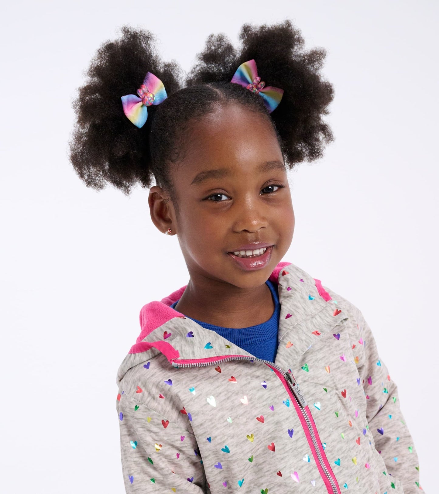 Lightweight zip-up rain jacket in gray with colorful confetti heart pattern and pink hood, worn by a smiling girl.