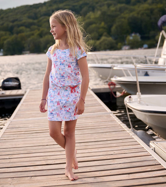 White t-shirt dress featuring a colorful sailboat print, short sleeves, and a relaxed fit, worn by a girl on a dock.