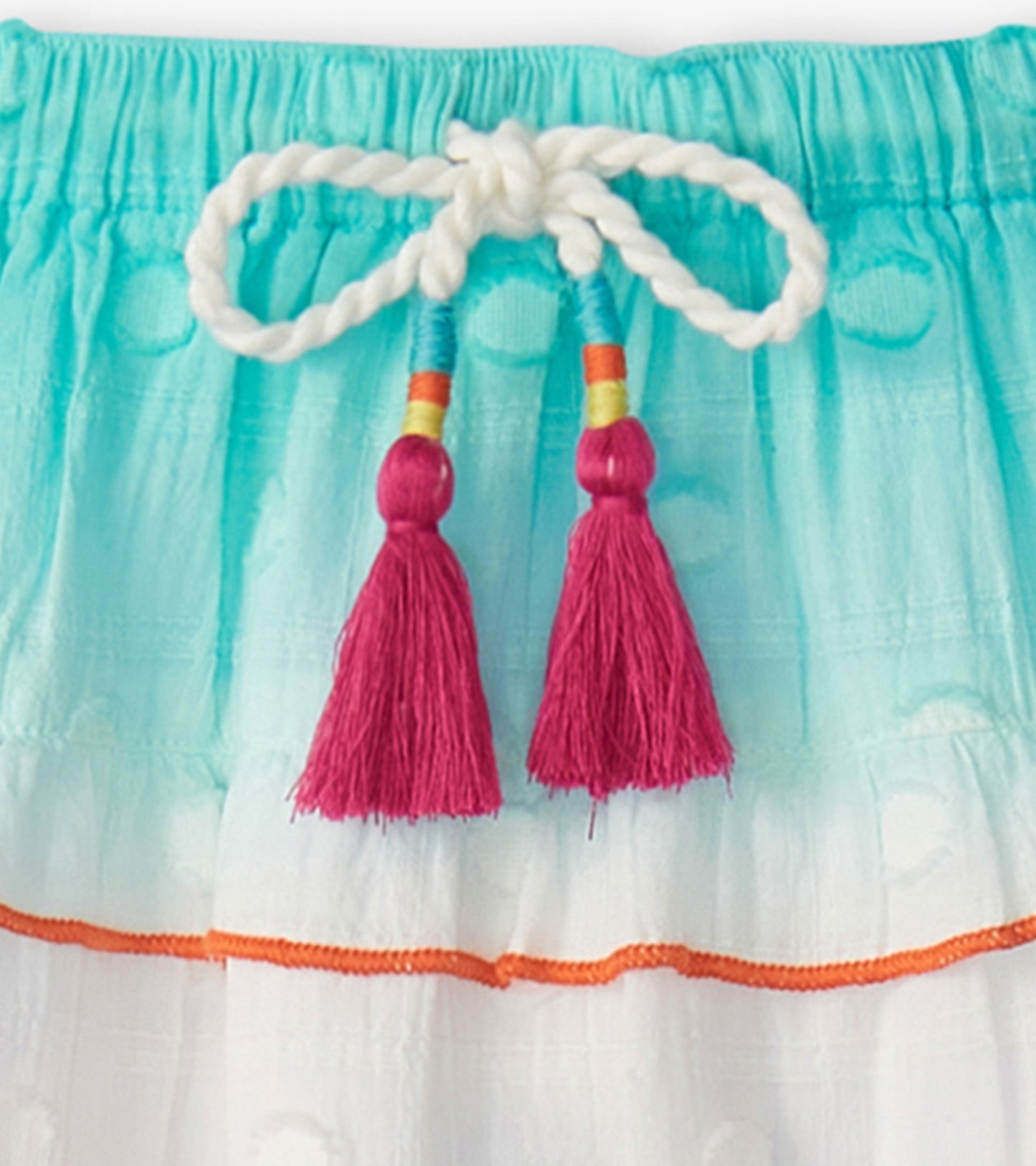 Tiered skirt featuring a gradient of turquoise to white, with colorful tassels and an orange trim at the hem.