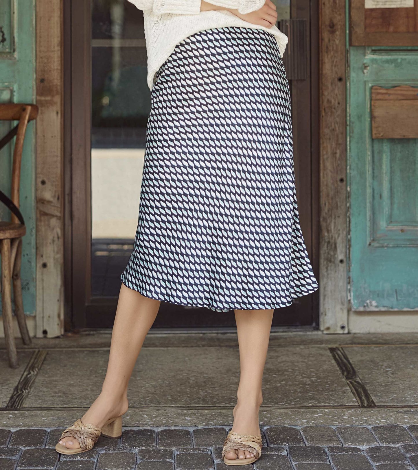Black midi skirt with a graphic leaf pattern, featuring a flared shape and lightweight fabric, styled with a casual top.