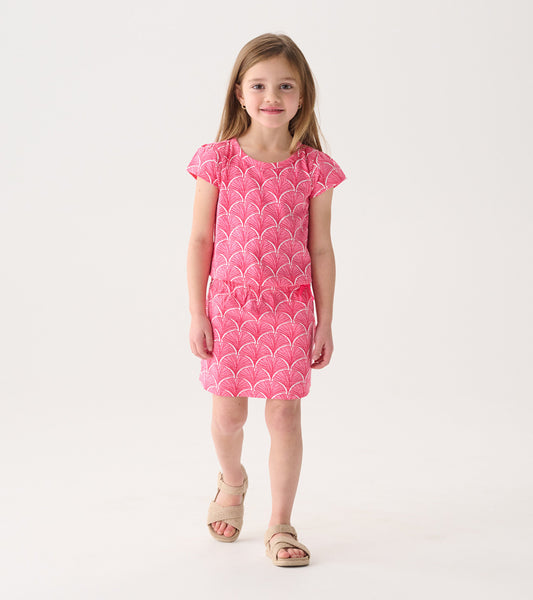 Coral pink T-shirt dress with a fan pattern, short sleeves, and a relaxed fit, worn by a girl standing.