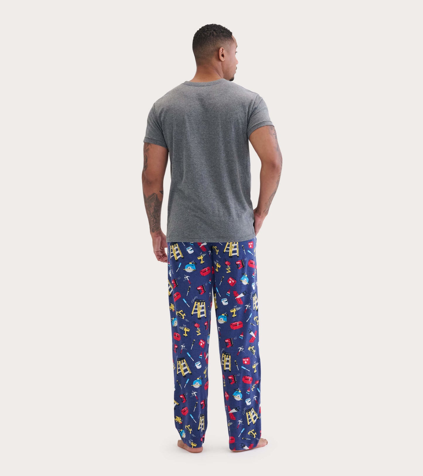 Gray short-sleeve tee worn with colorful pajama pants featuring a playful tool pattern. View from the back.