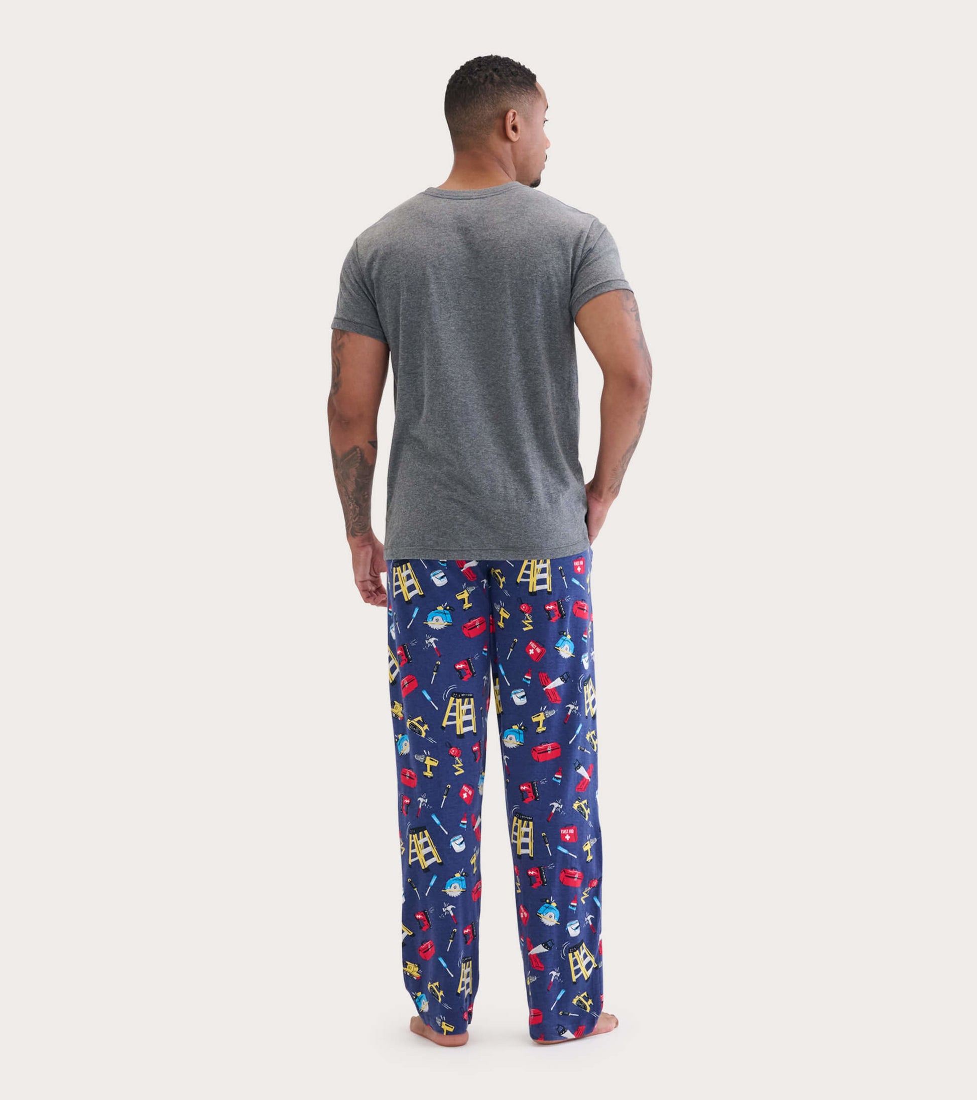 Gray short-sleeve tee worn with colorful pajama pants featuring a playful tool pattern. View from the back.