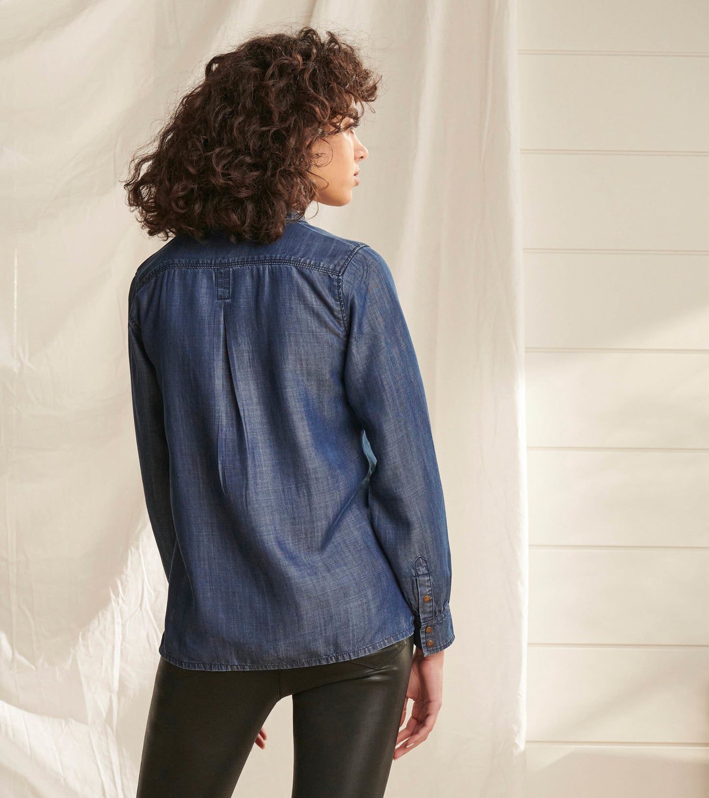 Denim button-down shirt in maritime wash, featuring a back pleat and long sleeves, styled with black leggings.