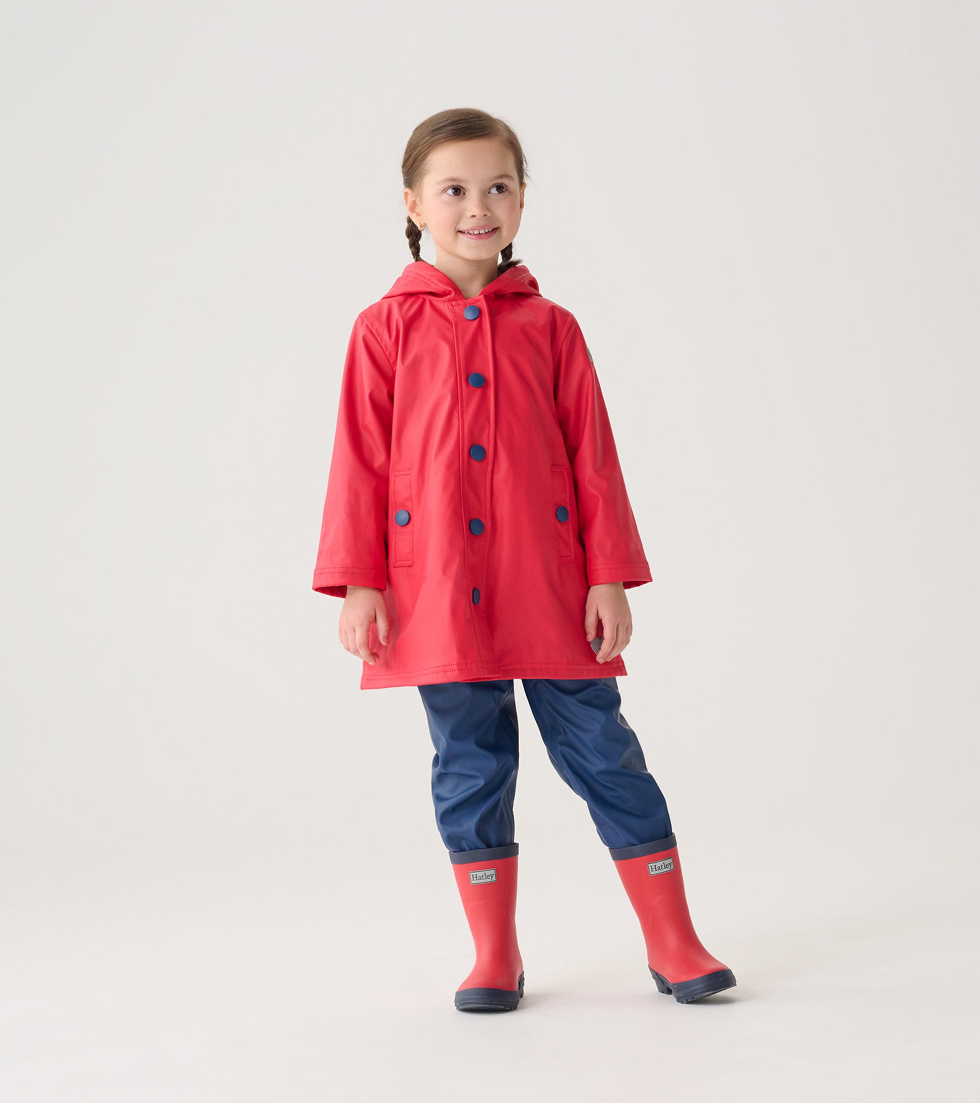 Red and navy button-up rain jacket with a hood, featuring blue buttons and pockets, worn by a smiling child.