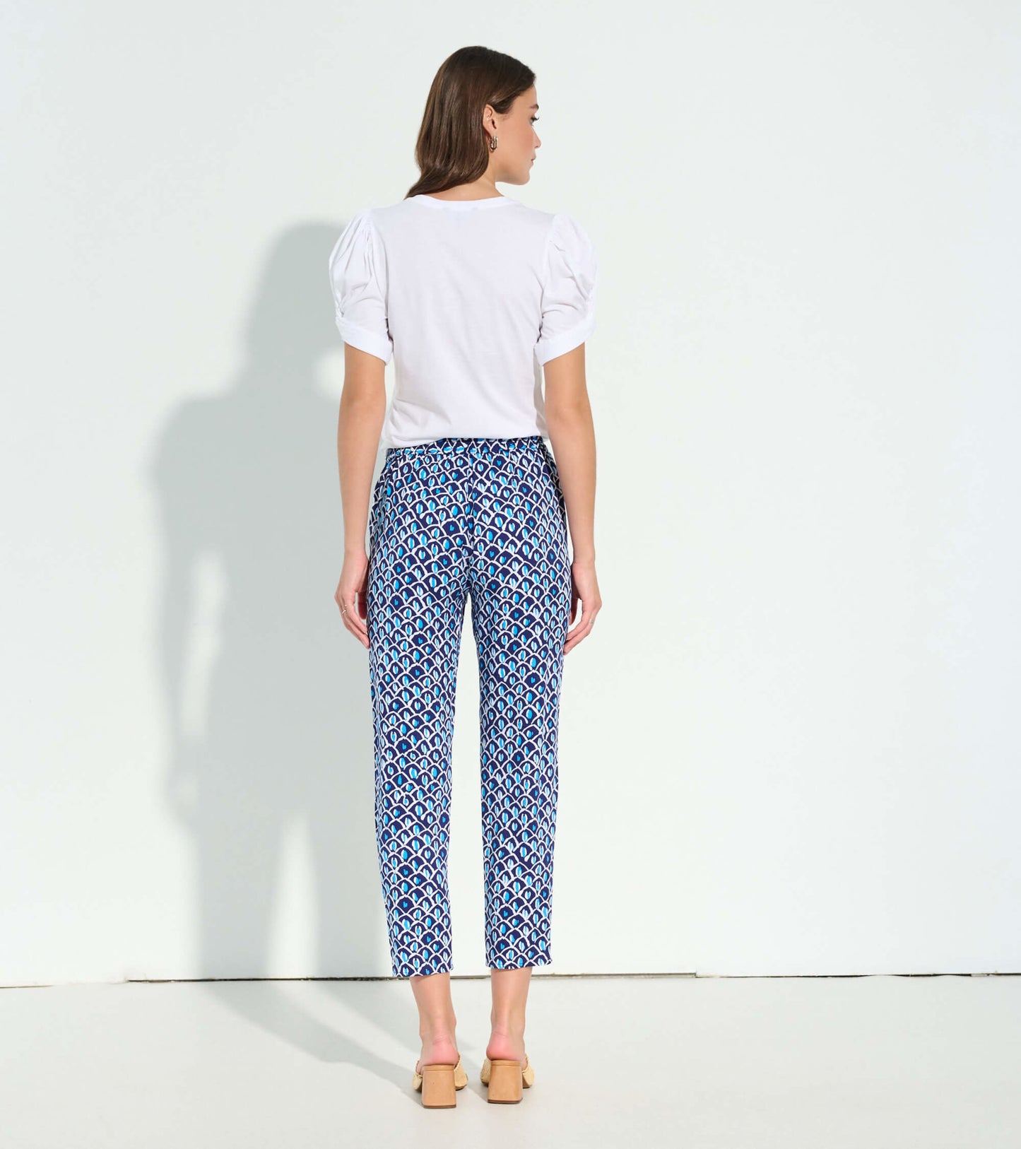 White short-sleeve tee with puffed sleeves, styled with patterned blue pants, viewed from the back.