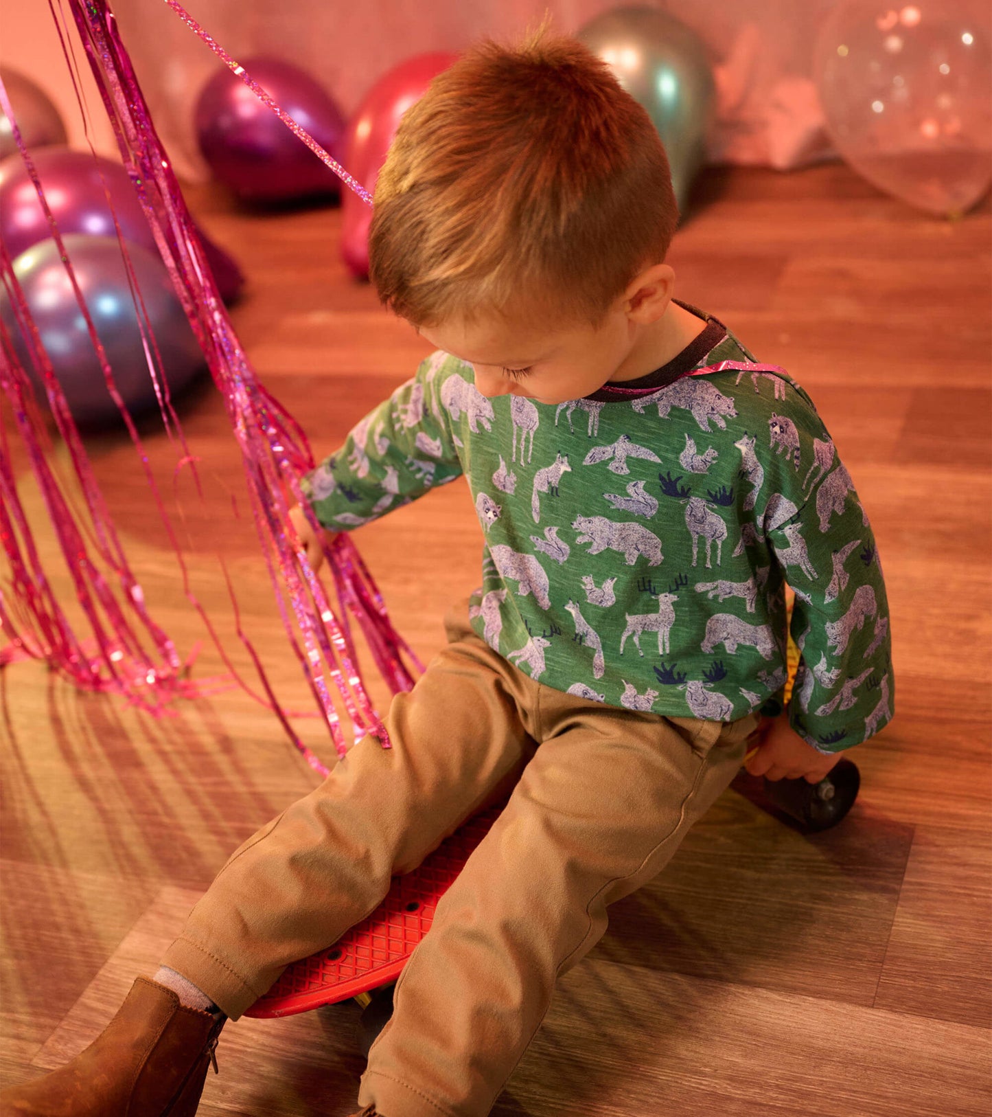 Green long sleeve t-shirt featuring various forest animals, worn by a child sitting on a skateboard.