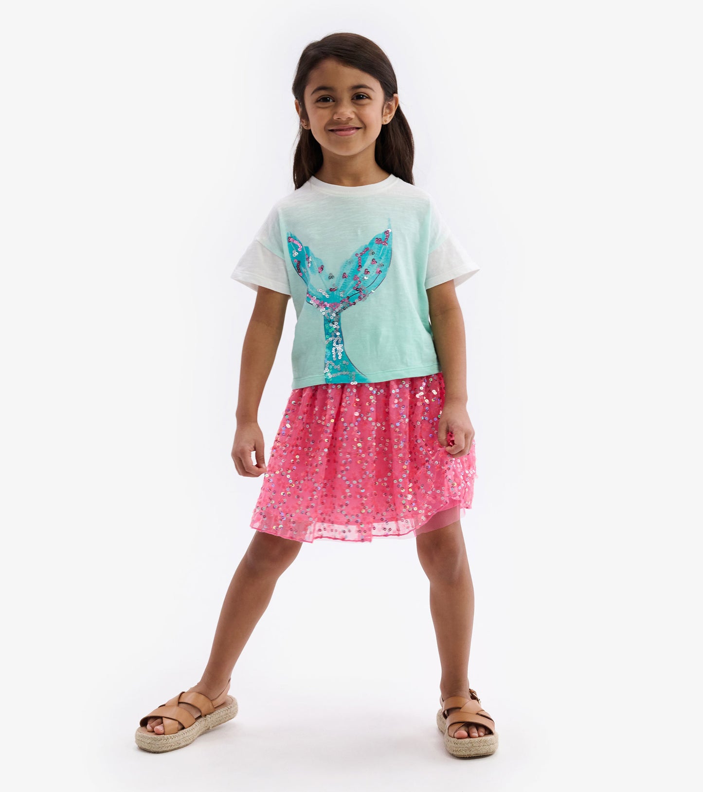 Light teal boxy tee with a whale tail graphic, paired with a pink sequined skirt, worn by a smiling girl.