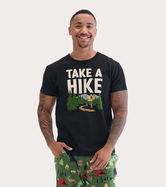Black short-sleeve tee featuring "Take A Hike" graphic with trees and a trail design, worn by a smiling man.