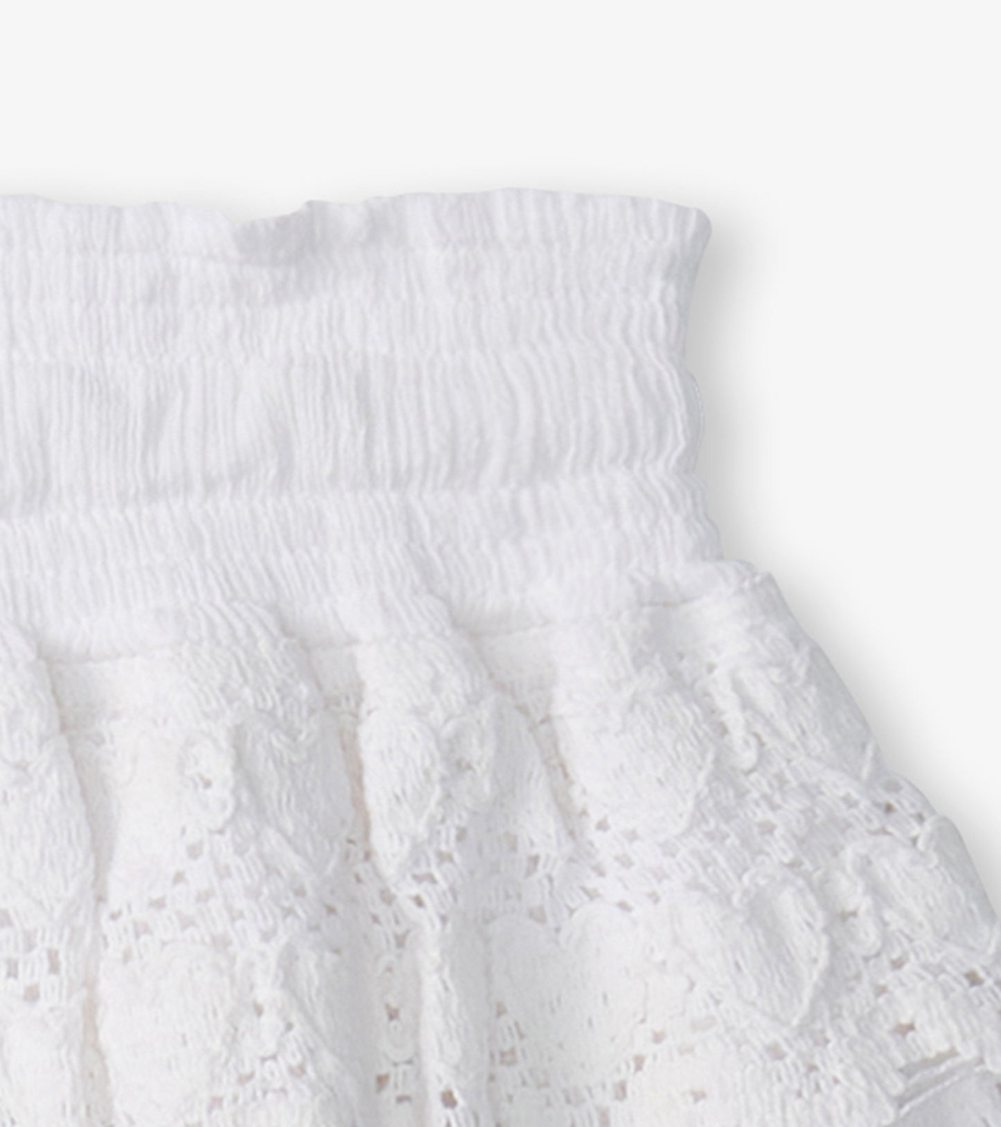White floaty skort featuring a smocked waistband and heart-shaped lace pattern. Ideal for casual summer wear.