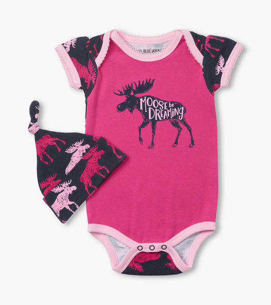 Pink baby bodysuit with moose graphic and navy patterned hat, featuring short sleeves and snap closure at the bottom.