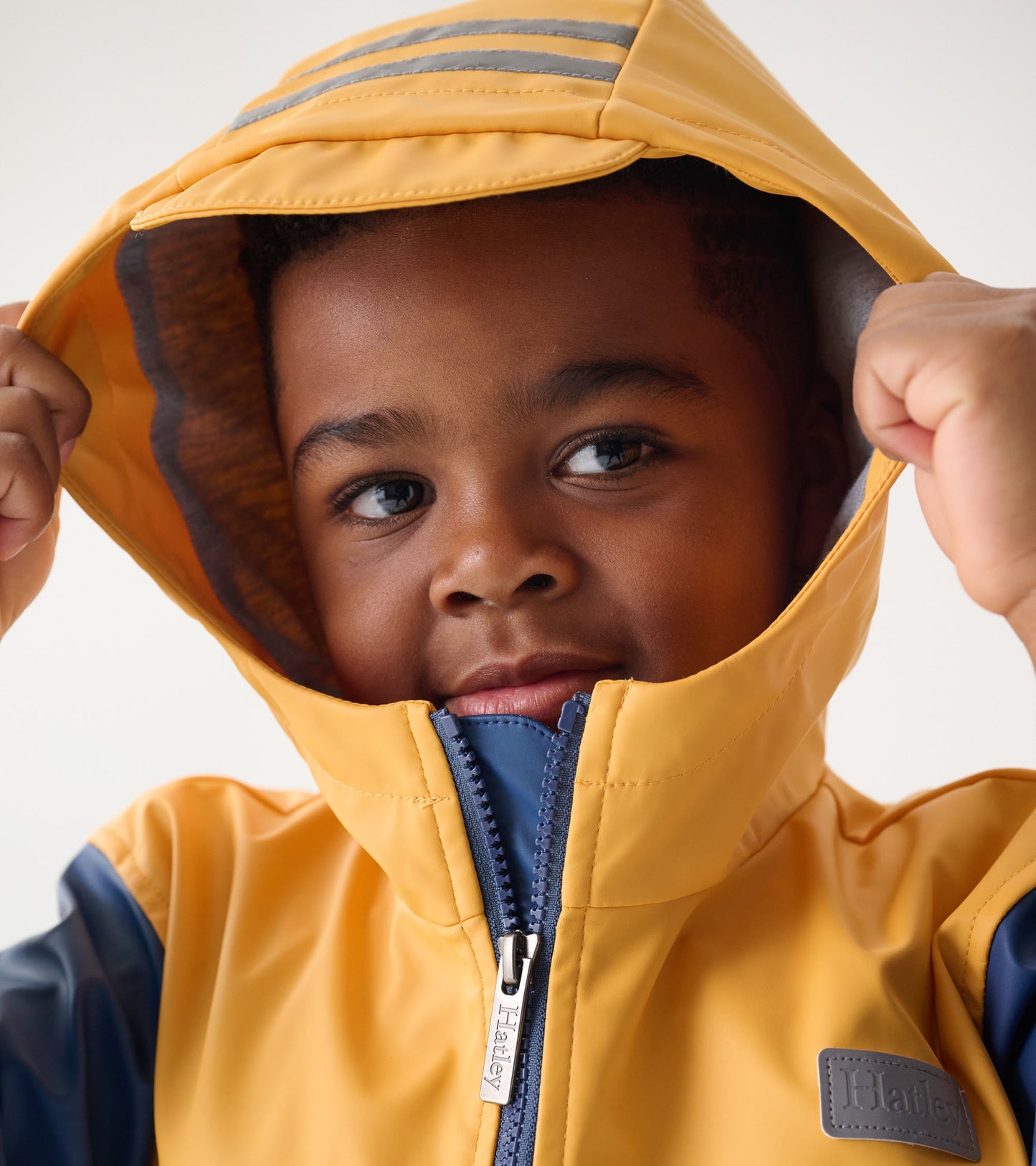 Yellow and navy zip-up rain jacket with a hood, featuring gray stripes and a front zipper, worn by a child.