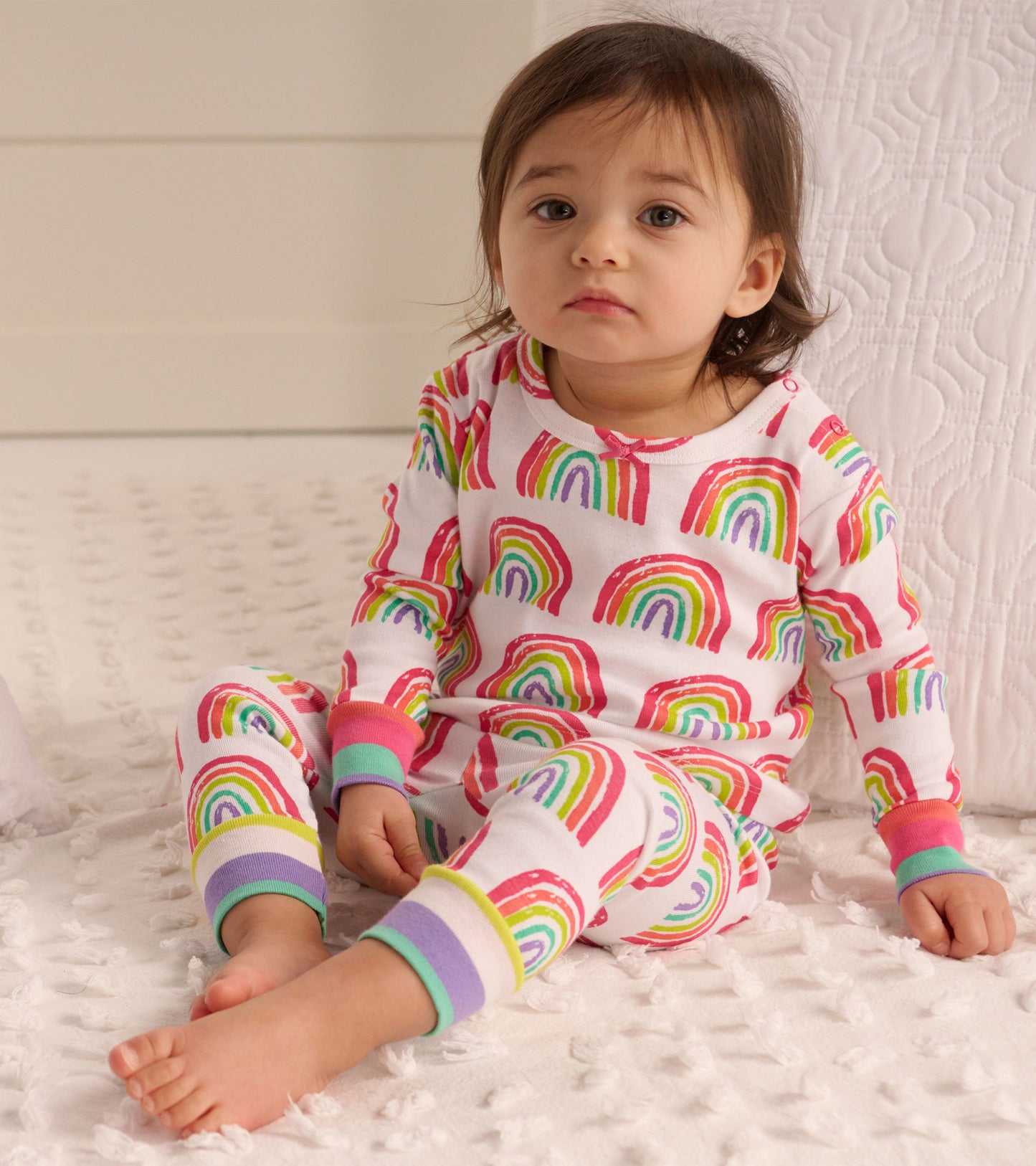 Organic cotton baby pajama set featuring colorful rainbow patterns, long sleeves, and matching pants with ribbed cuffs.