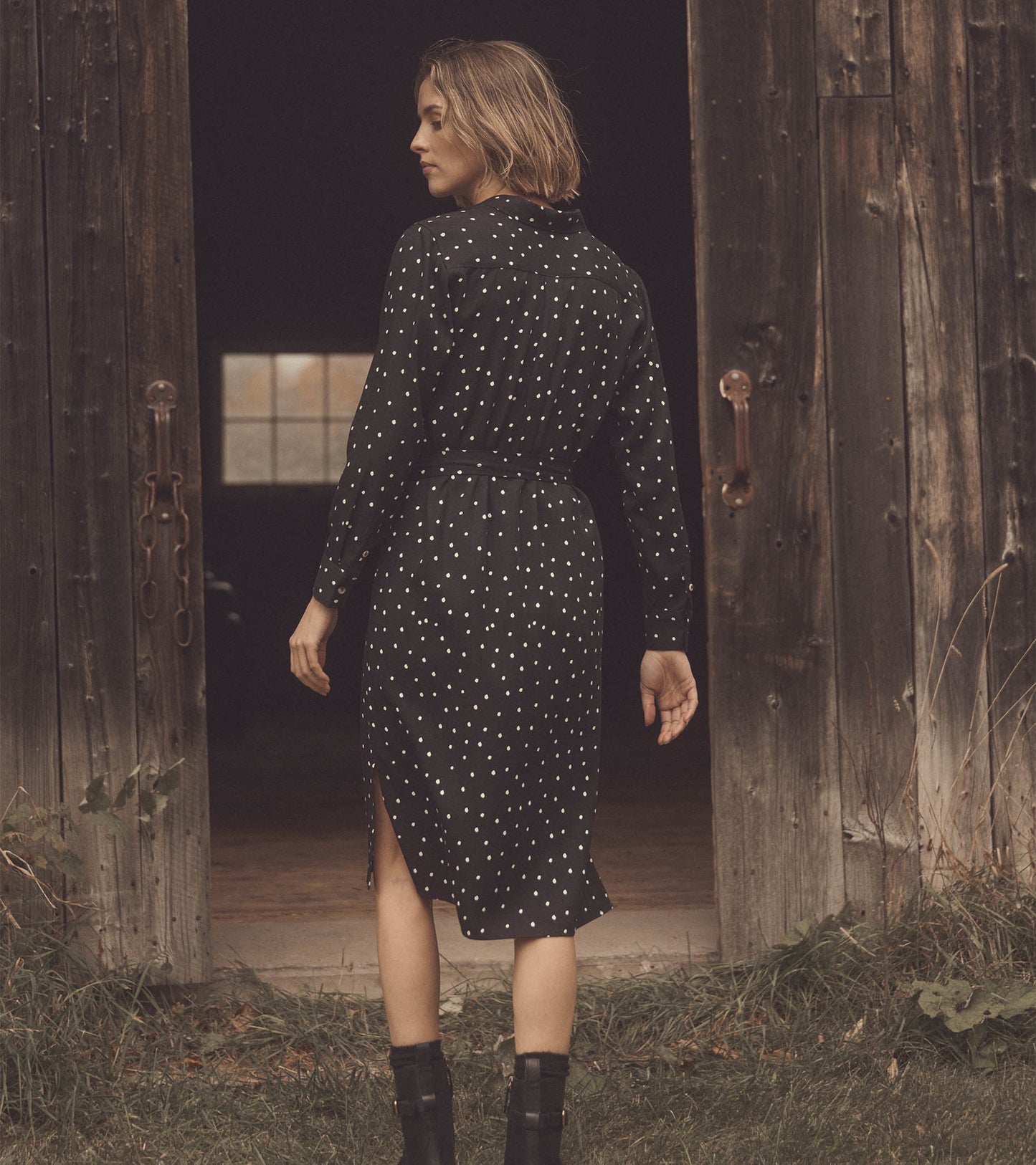 Black midi shirt dress with white spots, featuring a belted waist and side slit, styled with ankle boots.