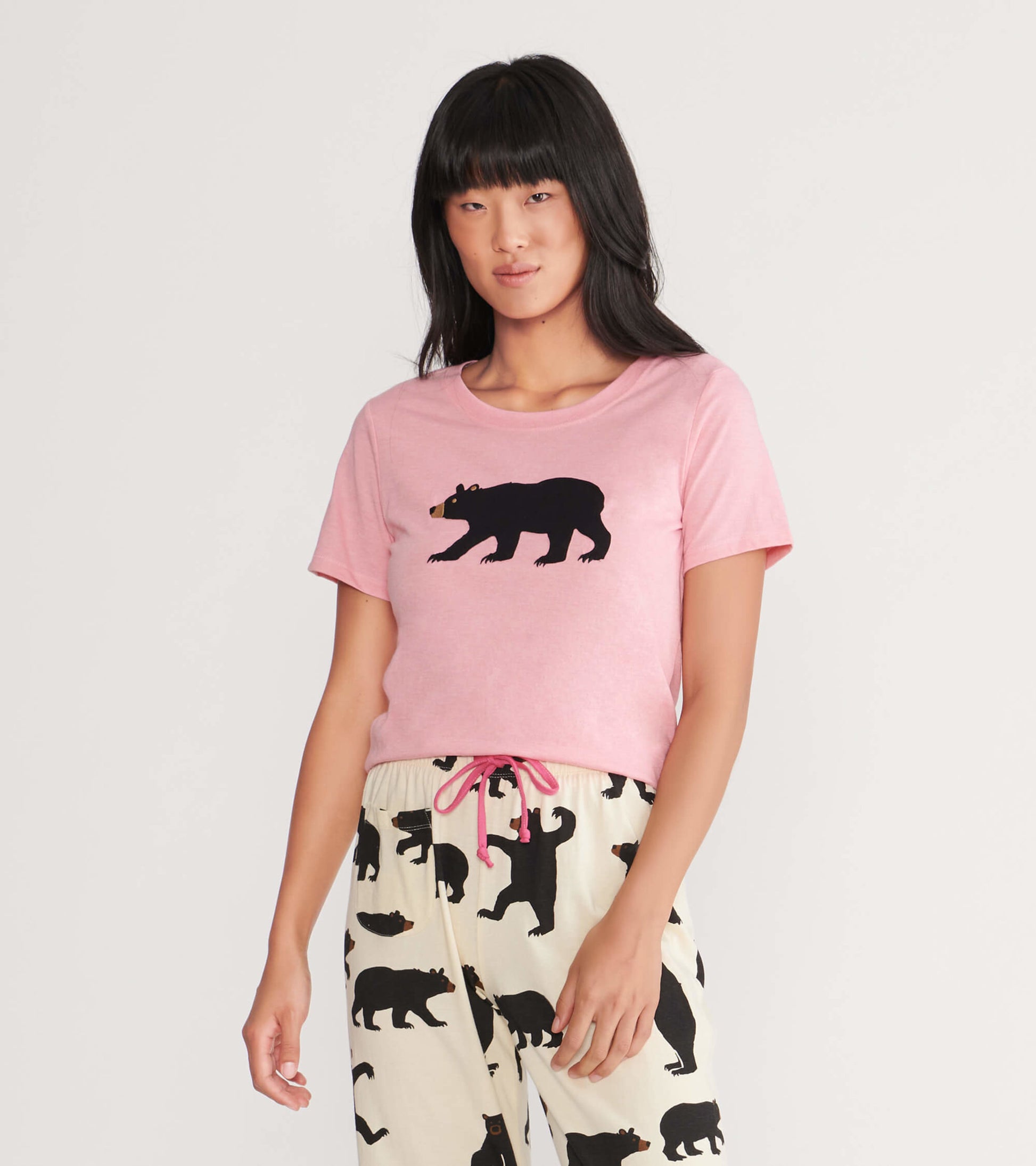 Pink women's pajama t-shirt featuring a black bear graphic, paired with patterned pajama pants.