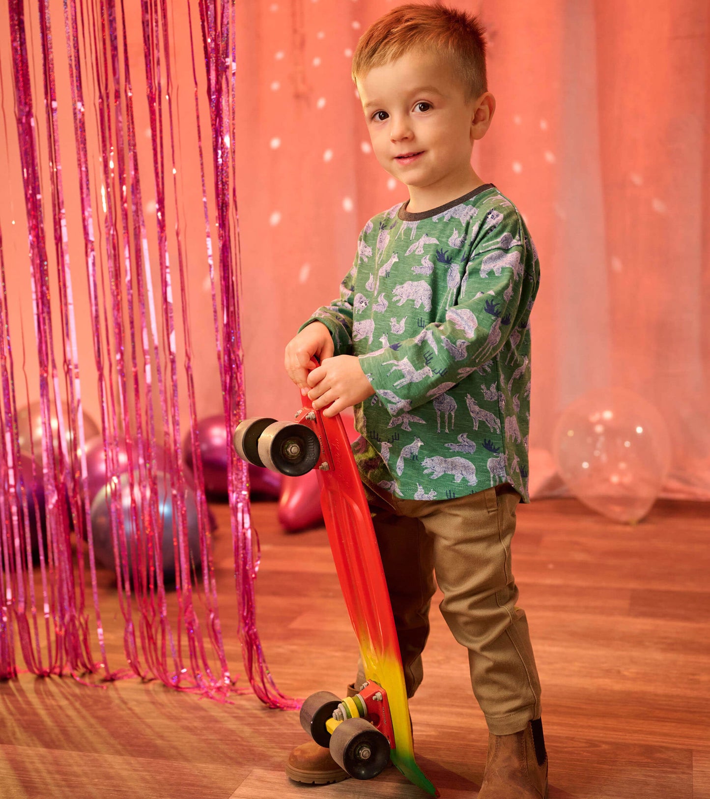 Green long sleeve t-shirt featuring a forest animal print, paired with tan pants and a red skateboard.