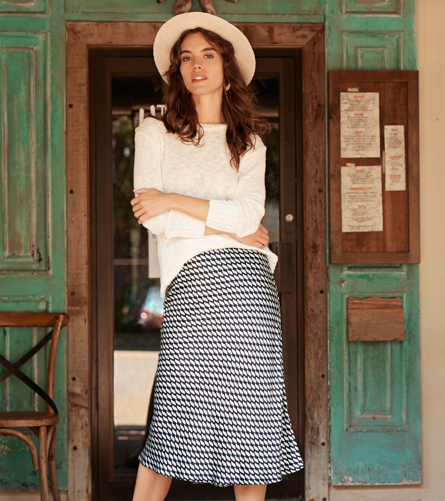 Black midi skirt with a graphic leaf pattern, featuring a flared silhouette, styled with a light sweater and hat.