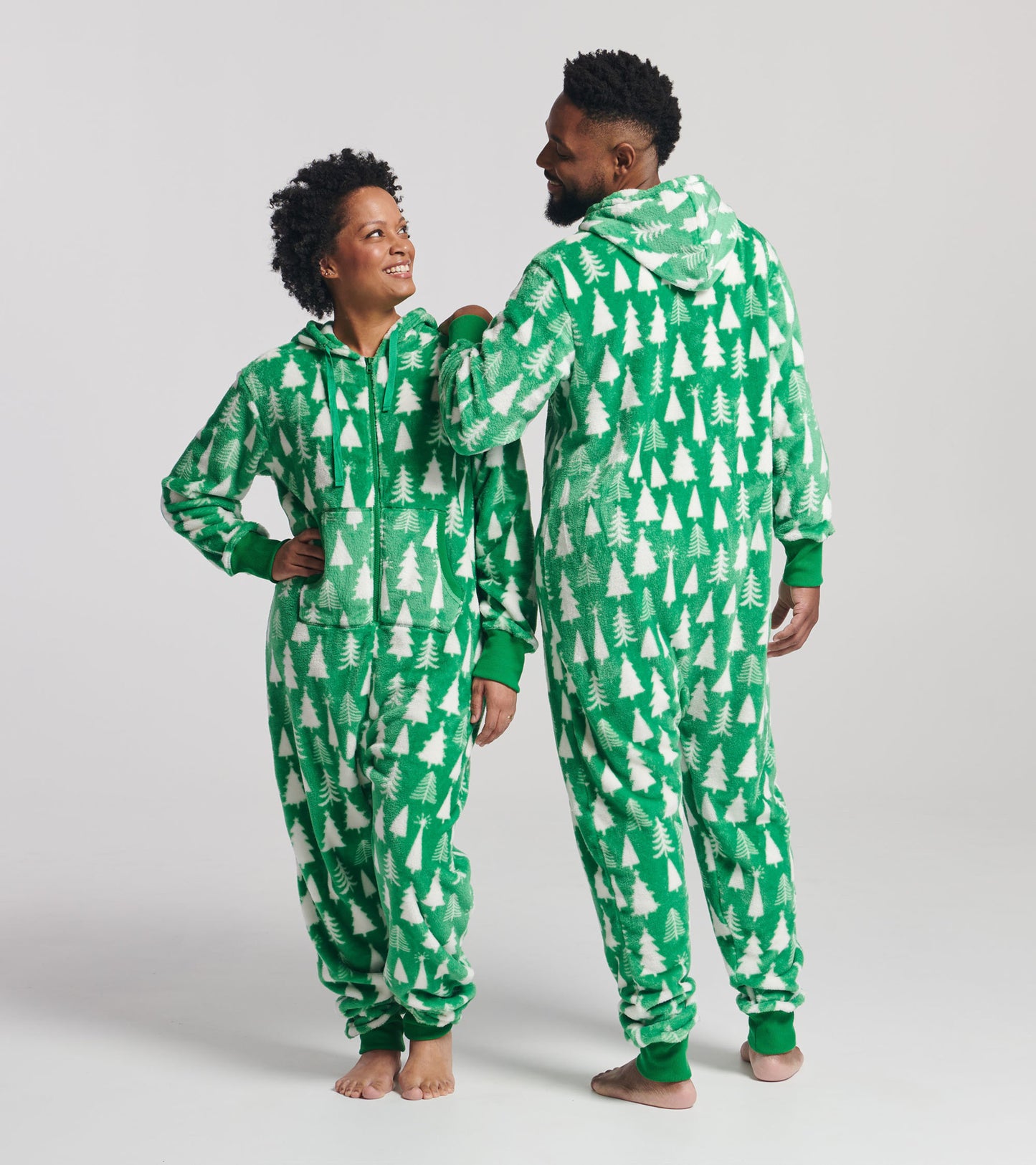 Green hooded fleece jumpsuit featuring a white tree pattern, worn by two people standing side by side.