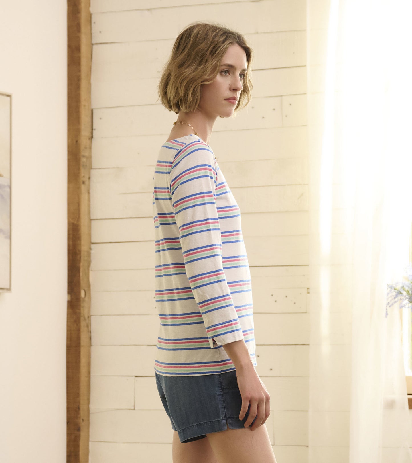 Long-sleeve top featuring a light background with colorful horizontal stripes, styled with denim shorts.