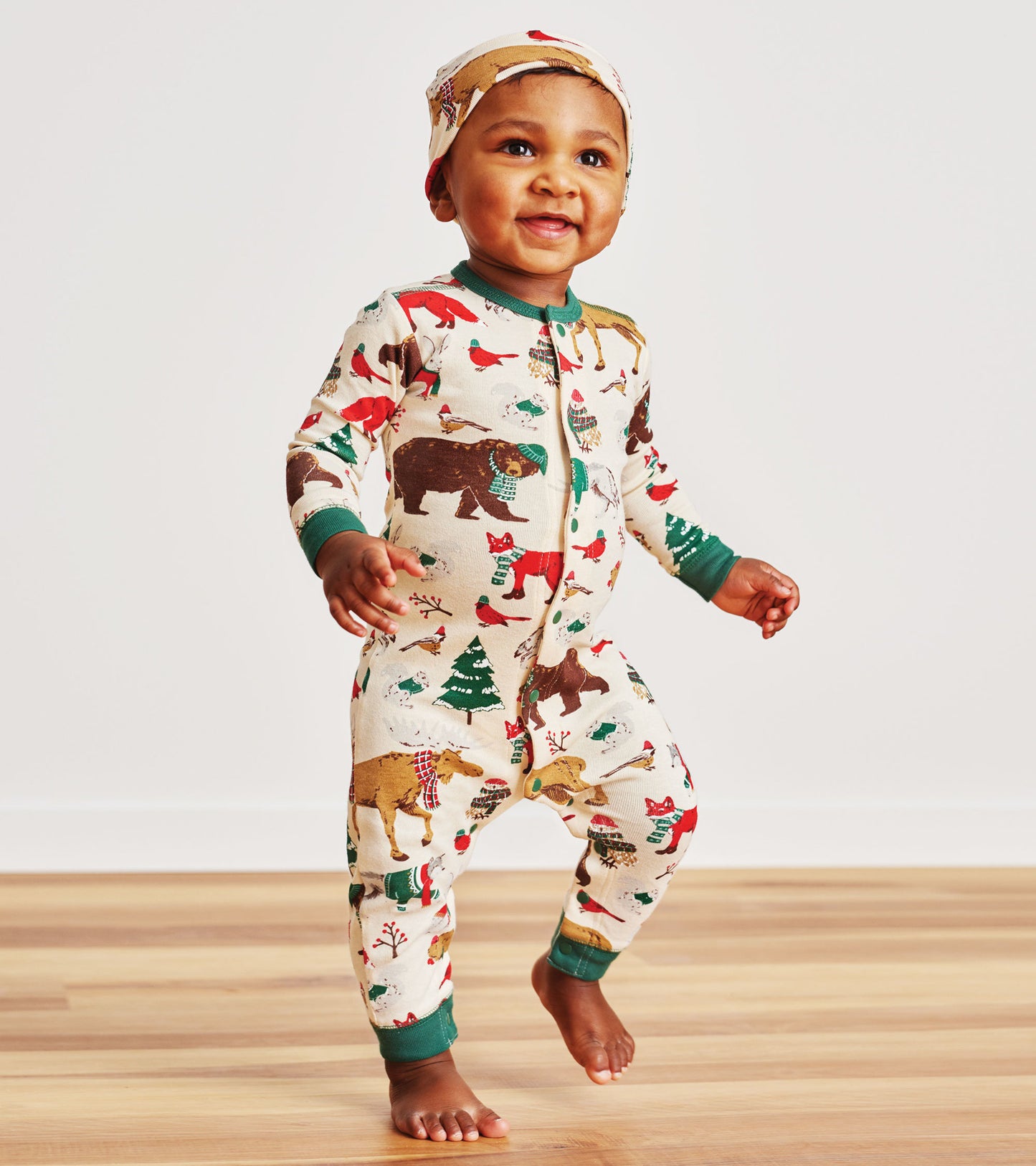 Cream-colored baby coverall with woodland animal prints, featuring a green trim and matching hat, suitable for winter wear.