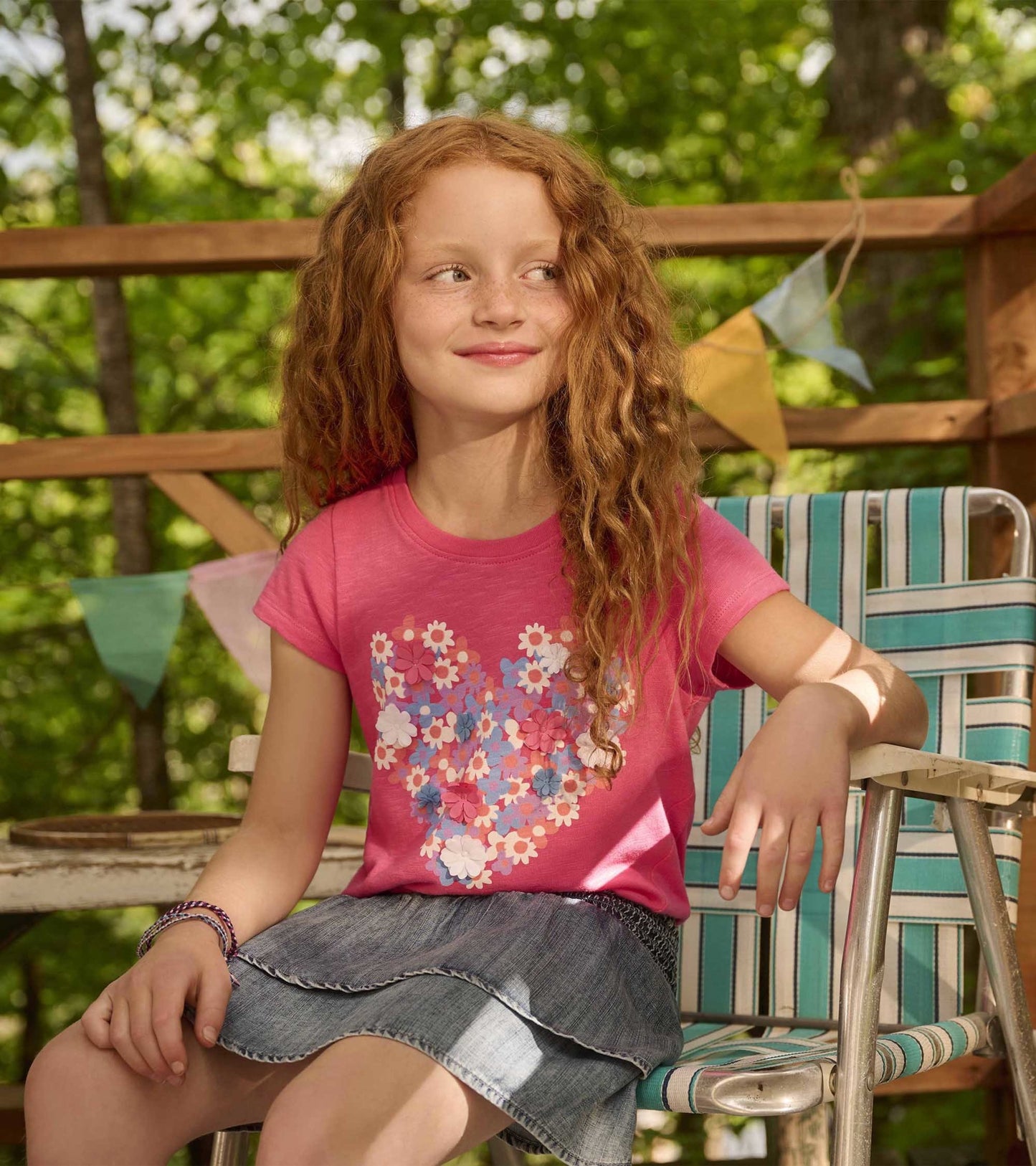Denim smocked skirt with layered ruffles, paired with a pink floral t-shirt, worn by a girl sitting on a chair.