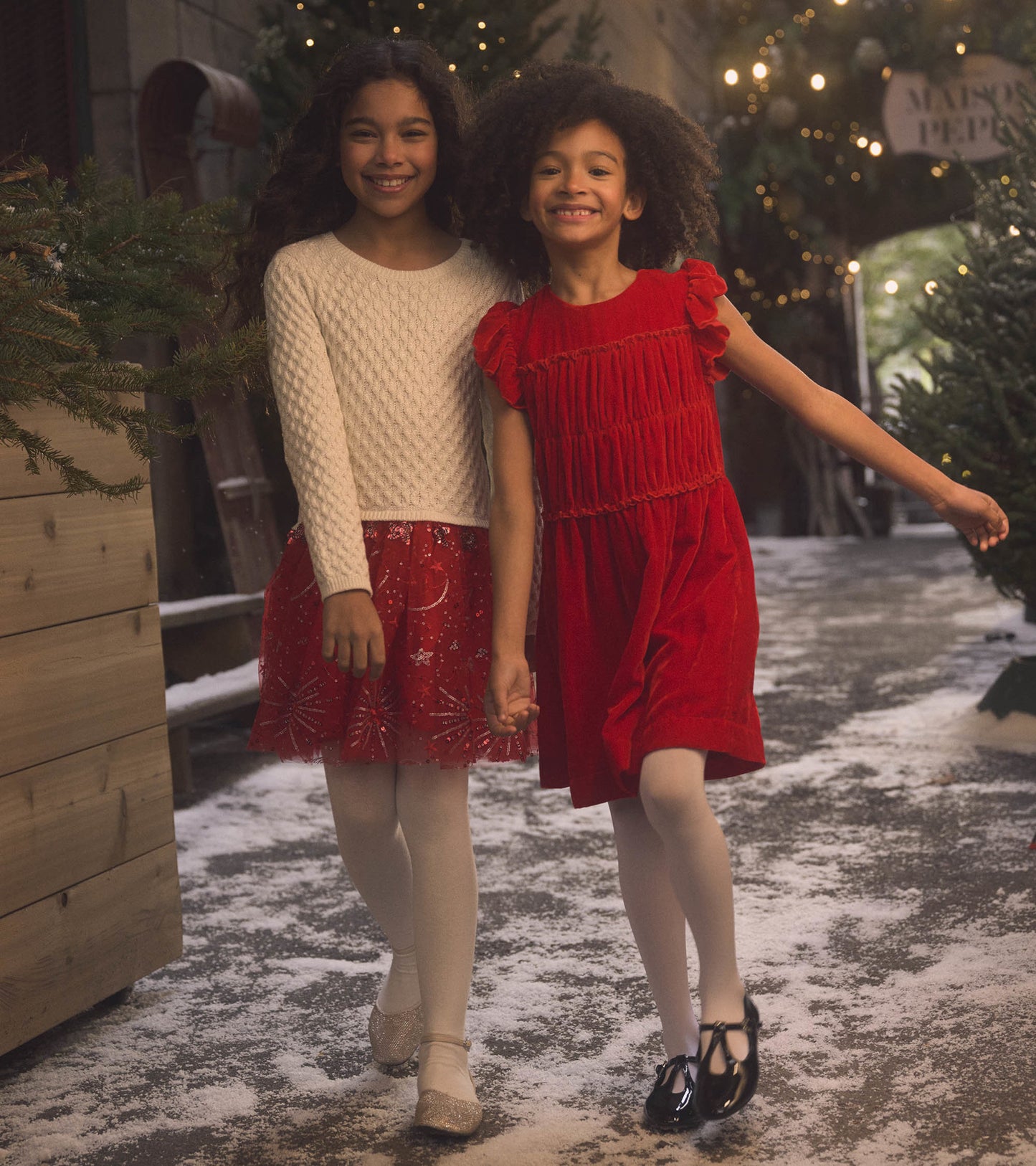 Red velvet smocked panel dress with ruffled sleeves, worn by a girl, paired with white tights and black shoes.