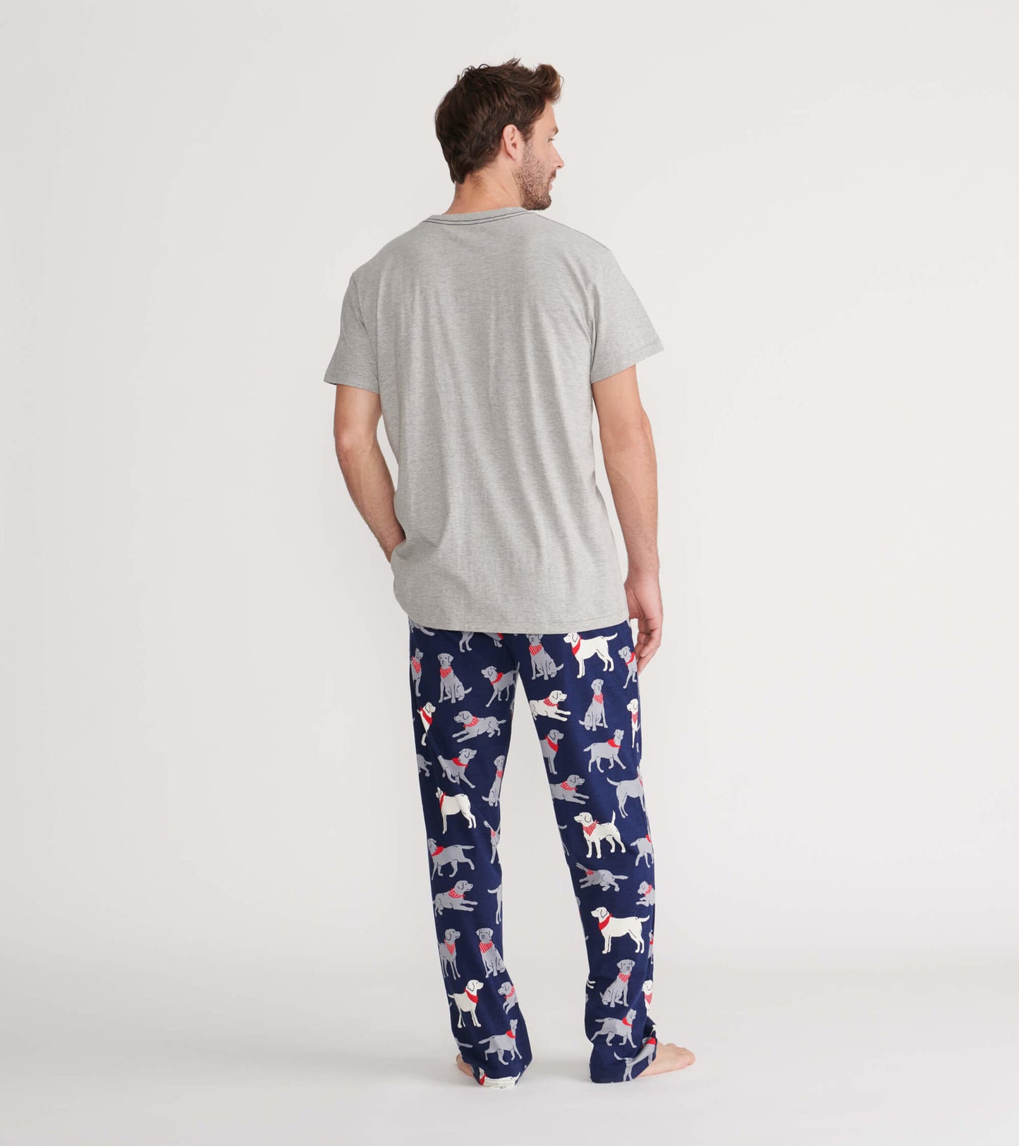 Gray short-sleeve men's tee worn with patterned pajama pants featuring colorful dog designs. View from the back.