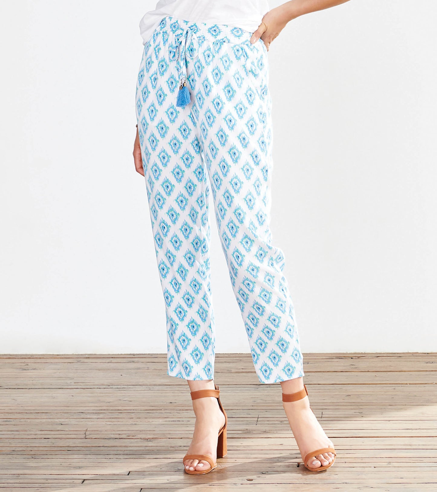 Lightweight, white pants with a blue diamond pattern and drawstring waist, styled with a casual top and heeled sandals.
