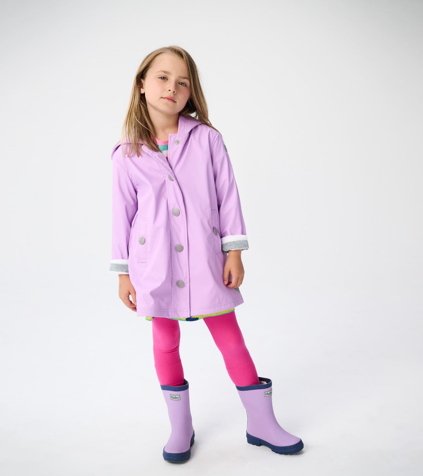 Lilac and navy matte rain boots with a rounded toe, worn by a child in a pink outfit and lilac raincoat.