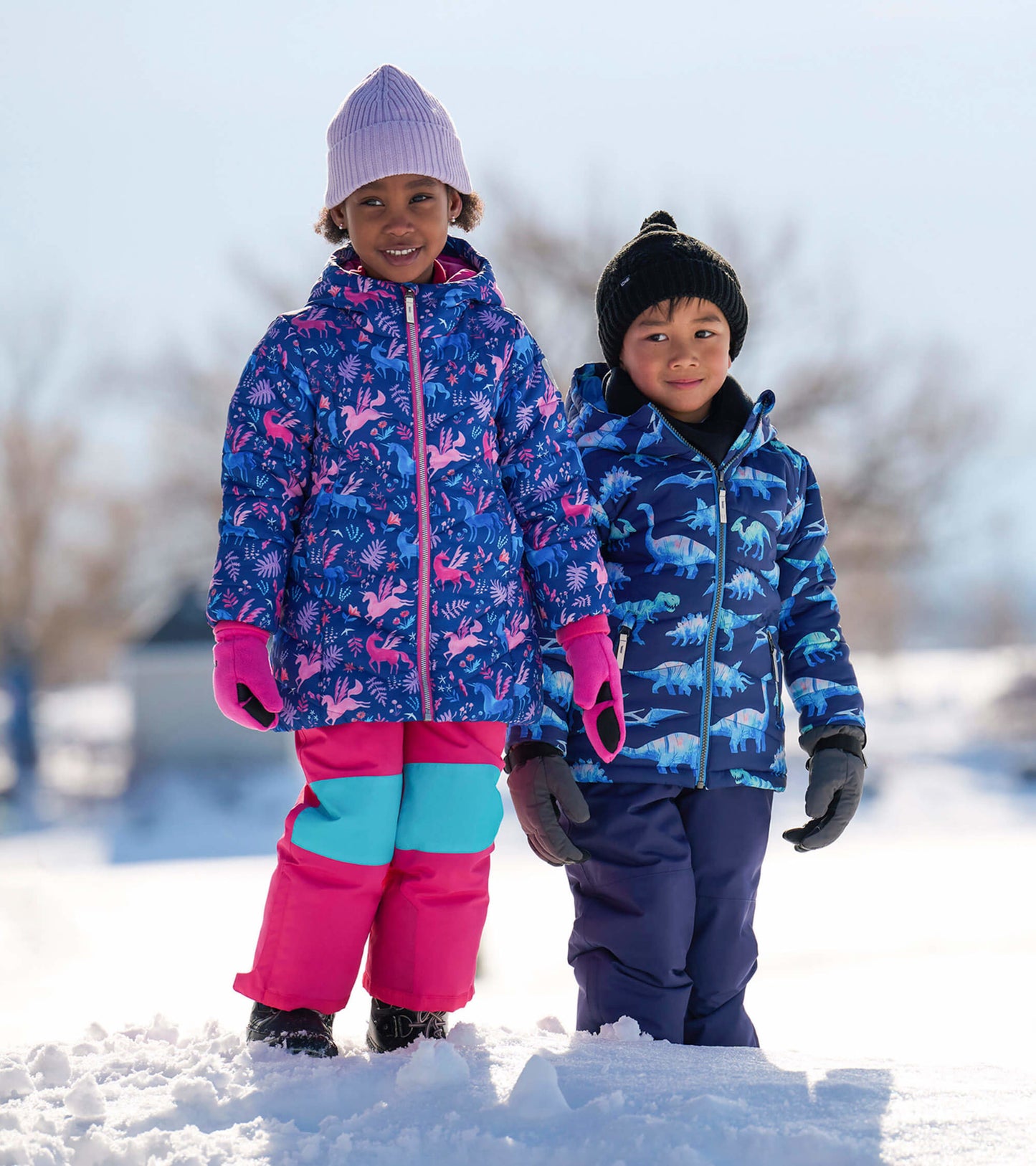 Colorful puffer jackets for kids, featuring playful patterns, worn by two children in winter attire standing in snow.