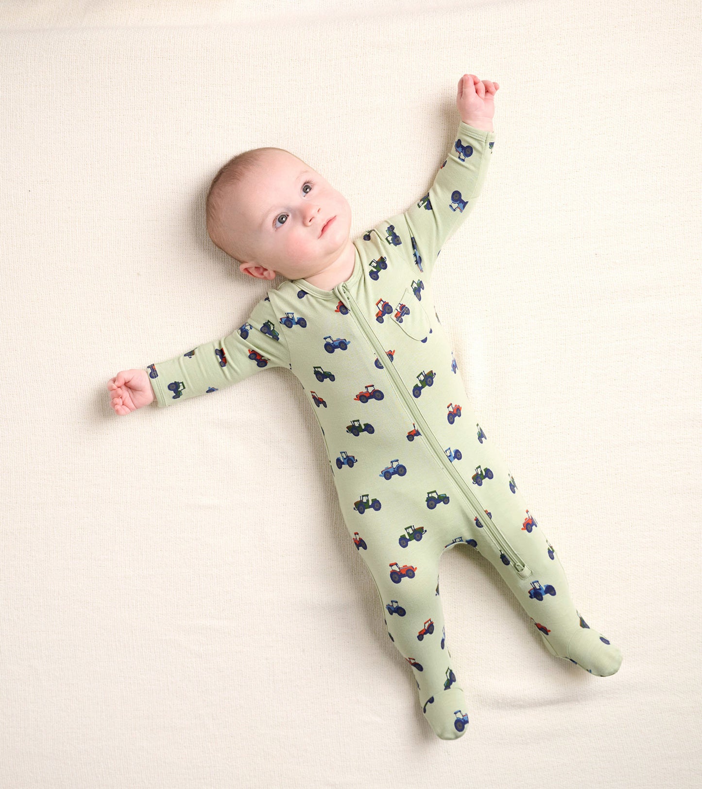 Light green zip-up footed sleeper featuring colorful tractor patterns, designed for newborns.