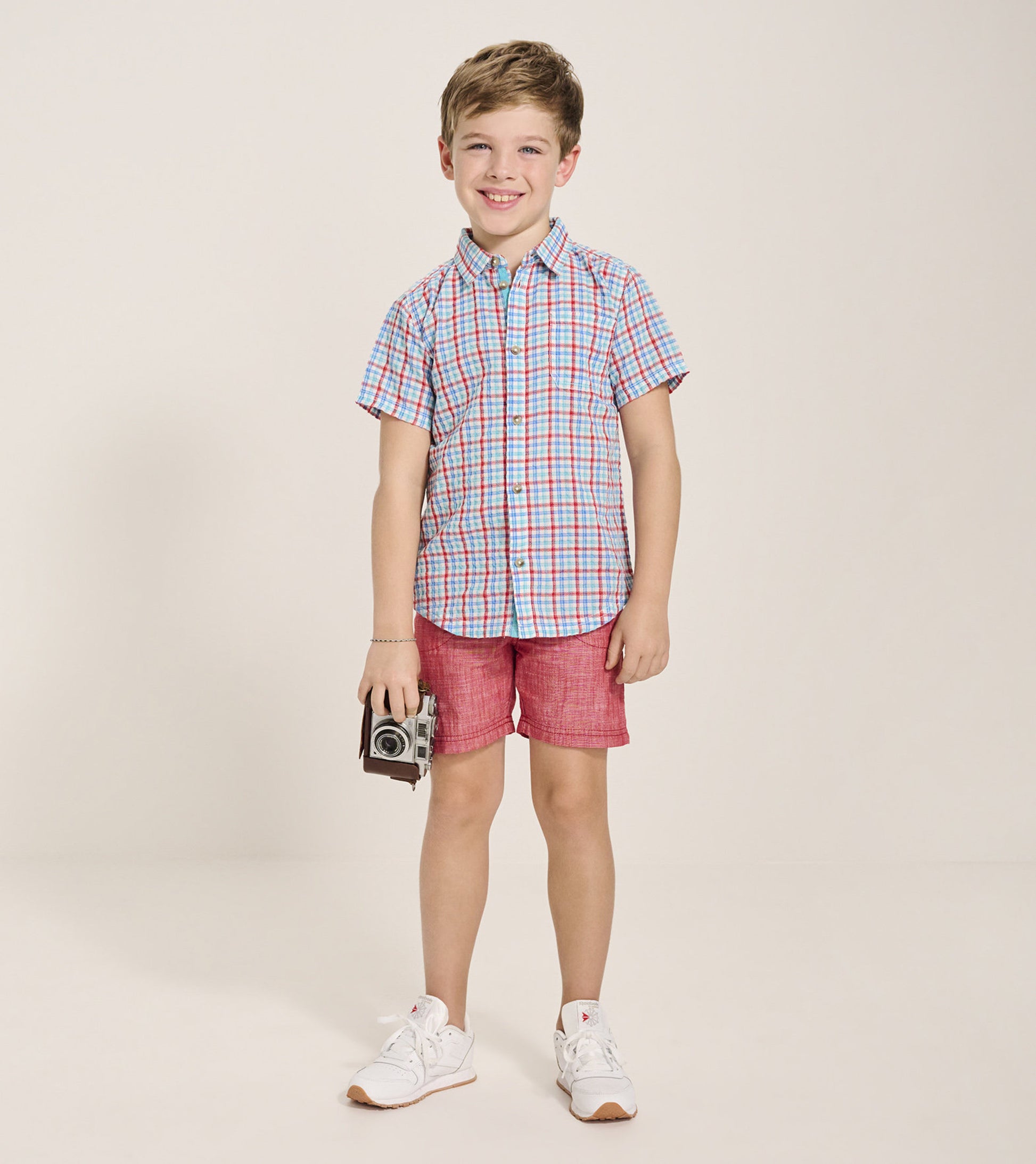 Short-sleeve button-down shirt featuring a blue, red, and white check pattern, worn with red shorts and white sneakers.