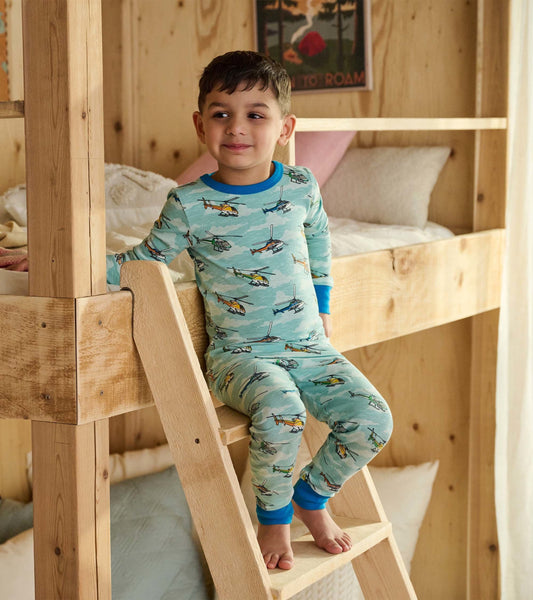 Light blue pajama set featuring colorful helicopter prints, with long sleeves and cuffs, worn by a boy sitting on a bunk bed…