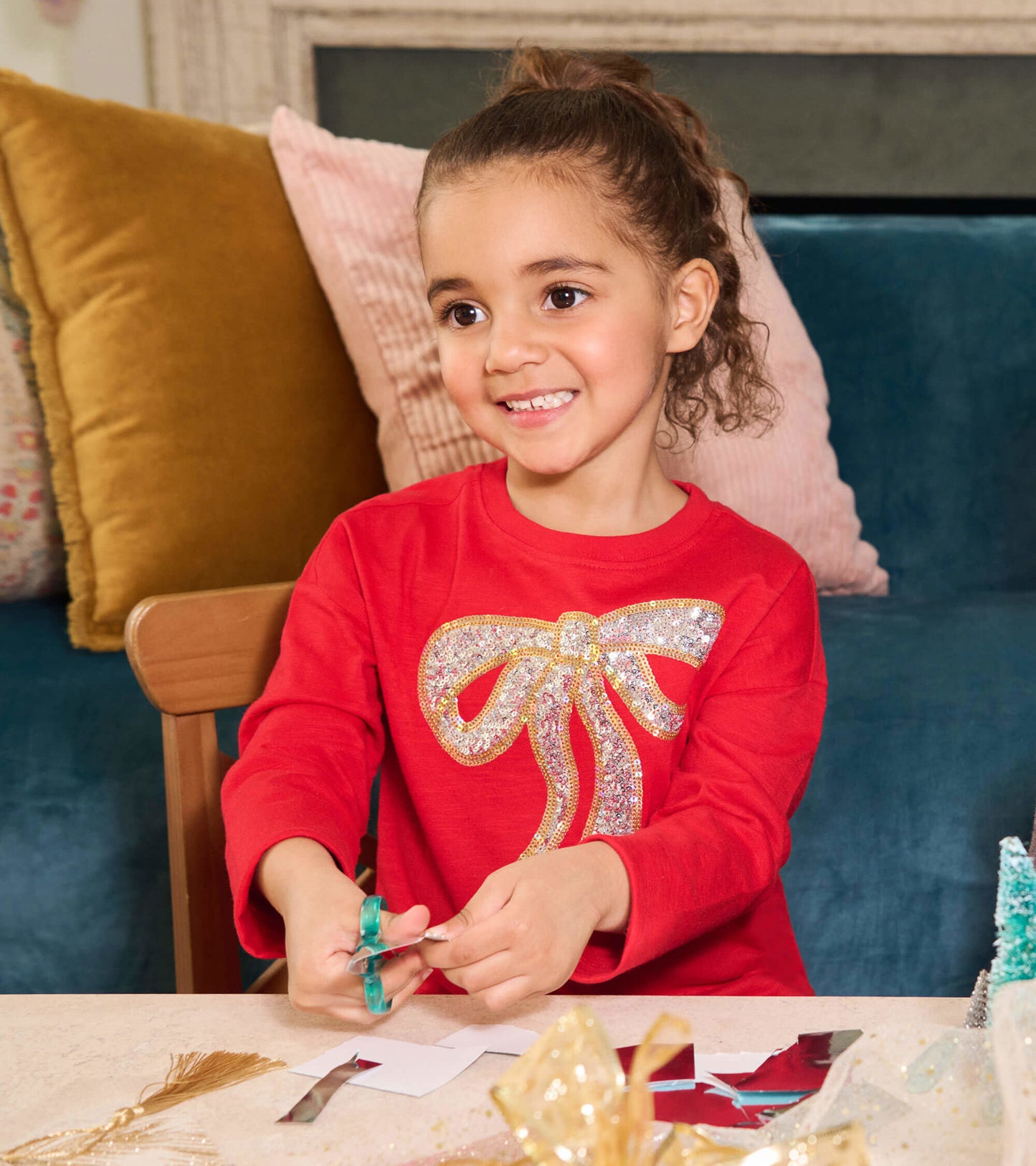 Red long-sleeve dress featuring a sparkling bow design, perfect for holiday parties, worn by a girl while crafting.