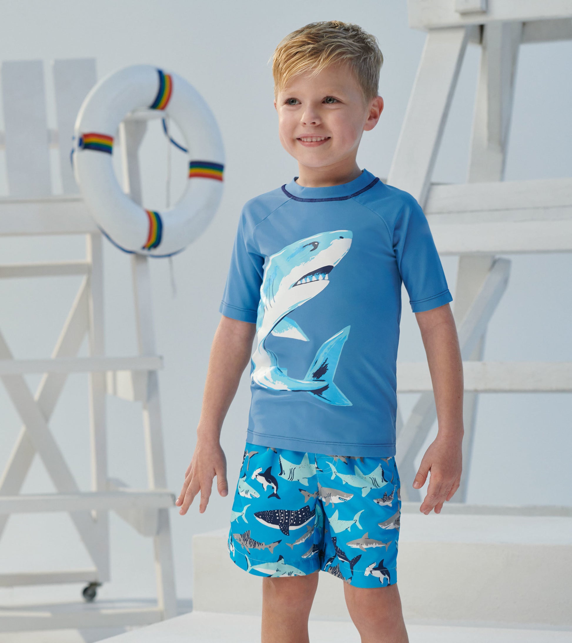 Light blue short sleeve rashguard featuring a shark graphic, paired with blue shorts adorned with shark patterns.